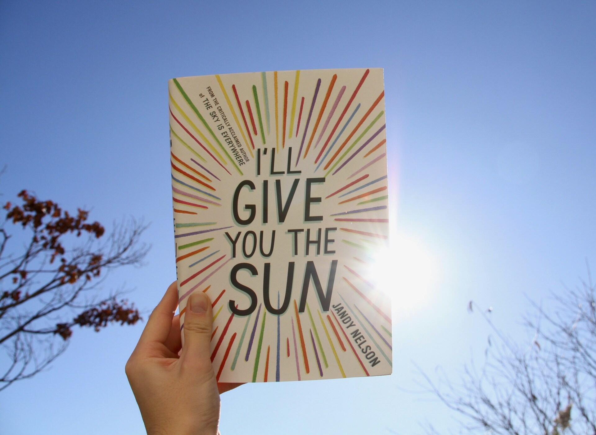 Książka pod tytułem „I'll give you the sun” w ręku na tle nieba.