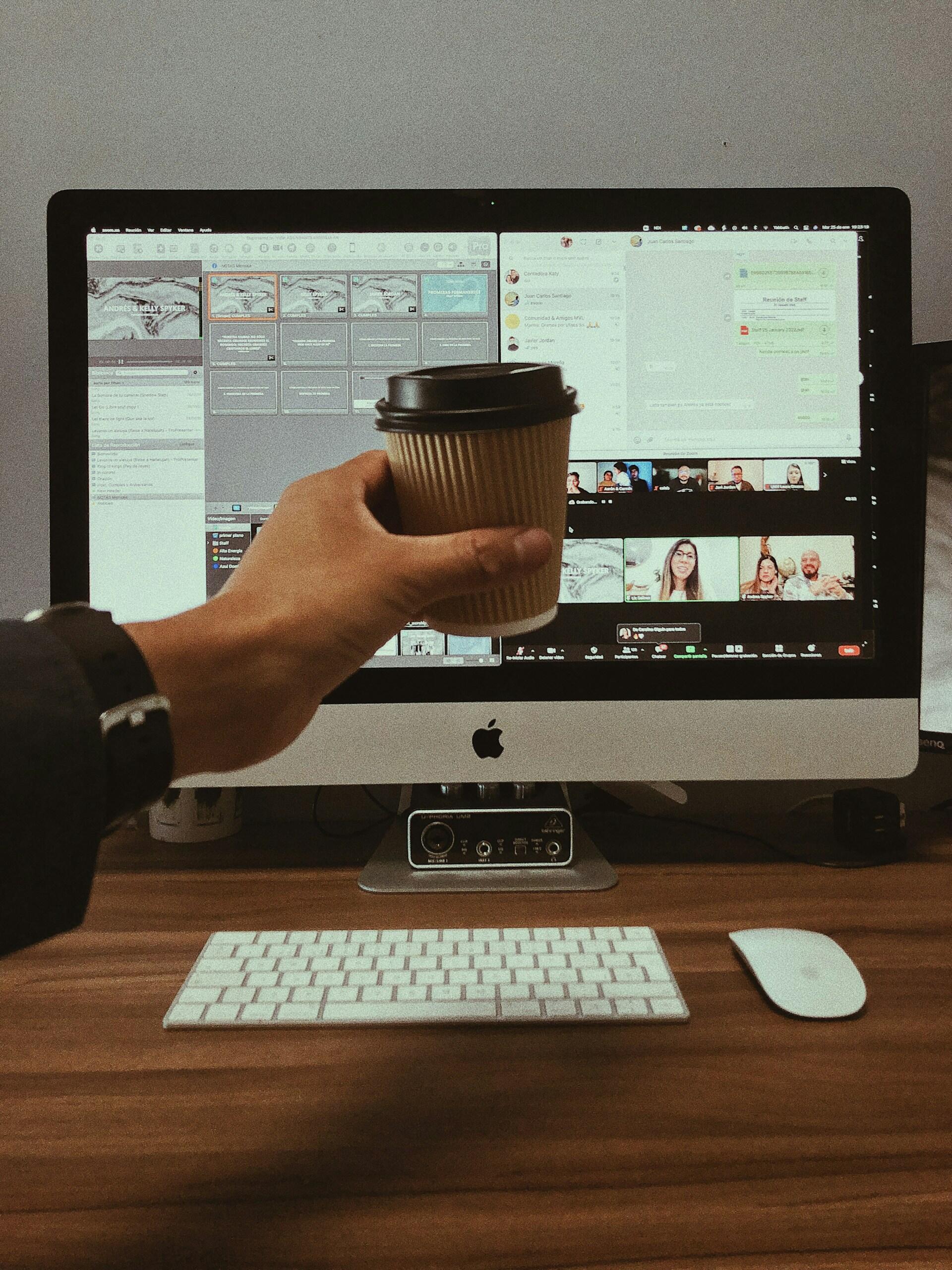 Dłoń z kubkiem kawy przy ekranie komputera ze spotkaniem online.