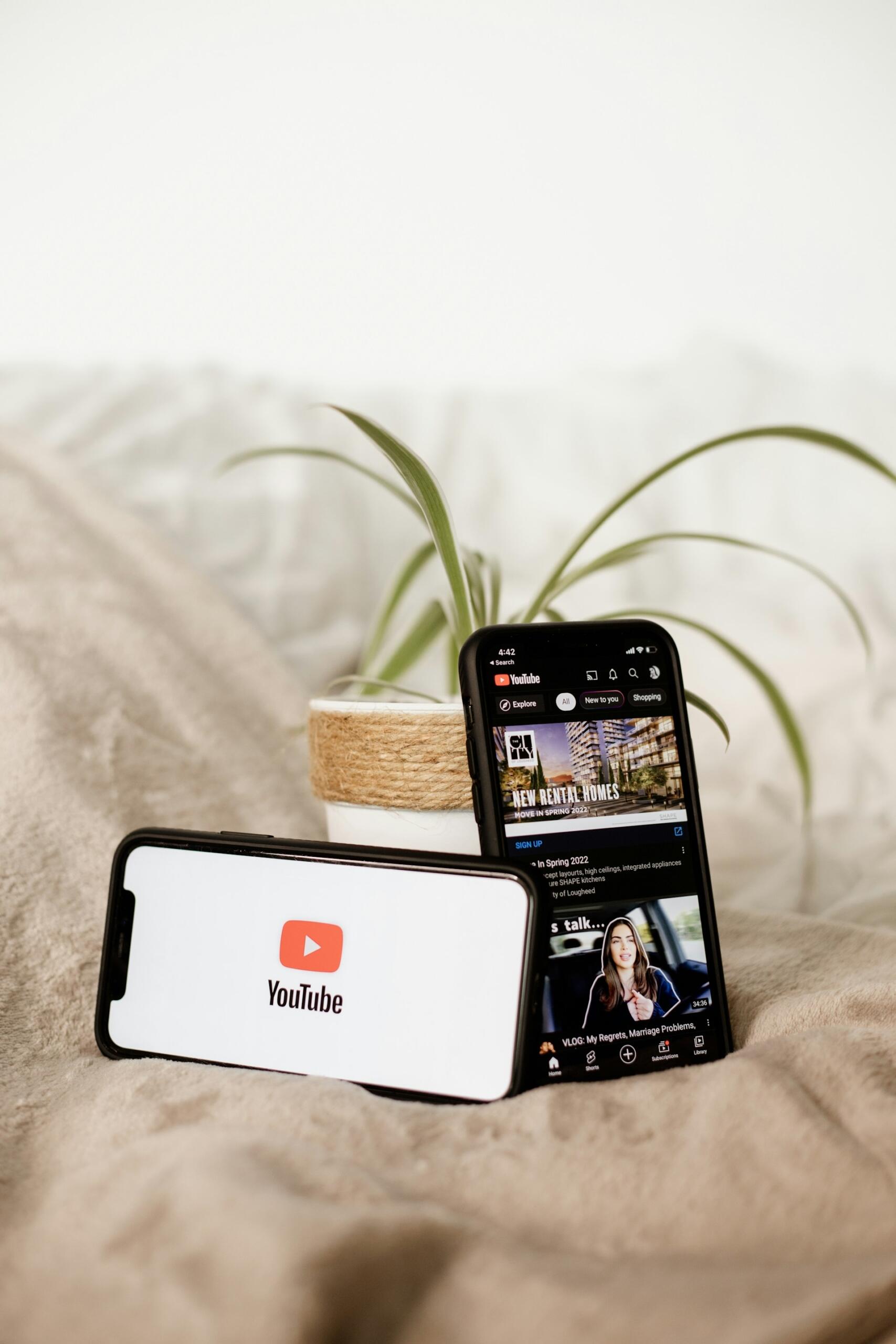 Youtube na telefonach przy roślinie doniczkowej na łóżku.