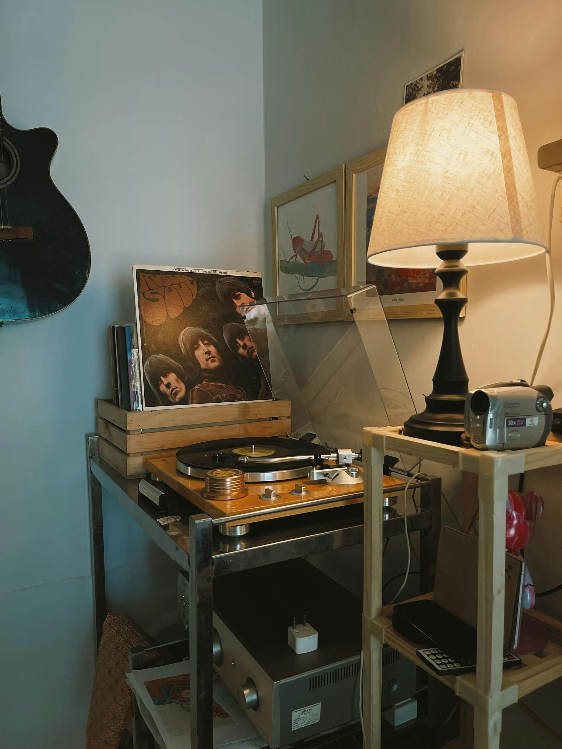 Gramofon na stoliku, płyta Beatlesów, lampa, kamera, gitara obrazy w niebieski pokoju.