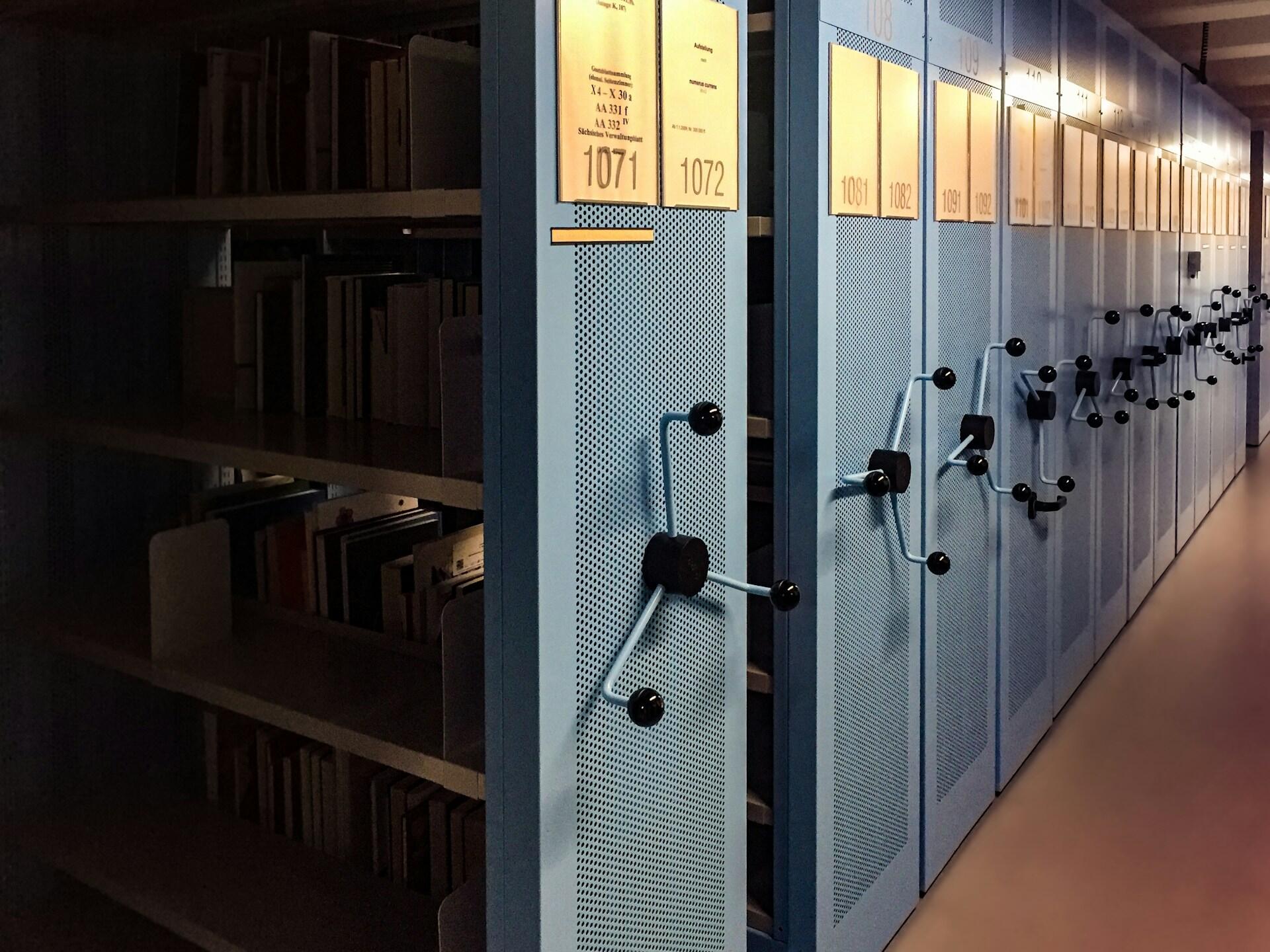 Wnętrze nowoczesnego archiwum lub magazynu bibliotecznego z przesuwanymi, metalowymi szafami / regałami zamontowanymi na szynach. Unsplash: C M