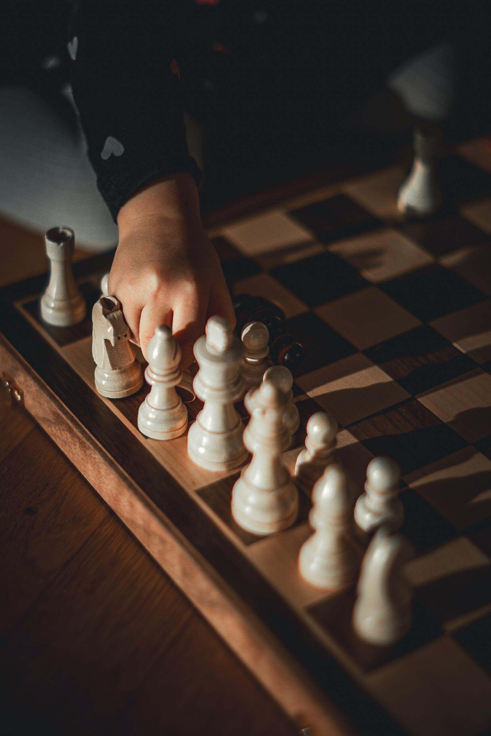 Dziecięca ręka przesuwająca białe figury na tablicy szachowej