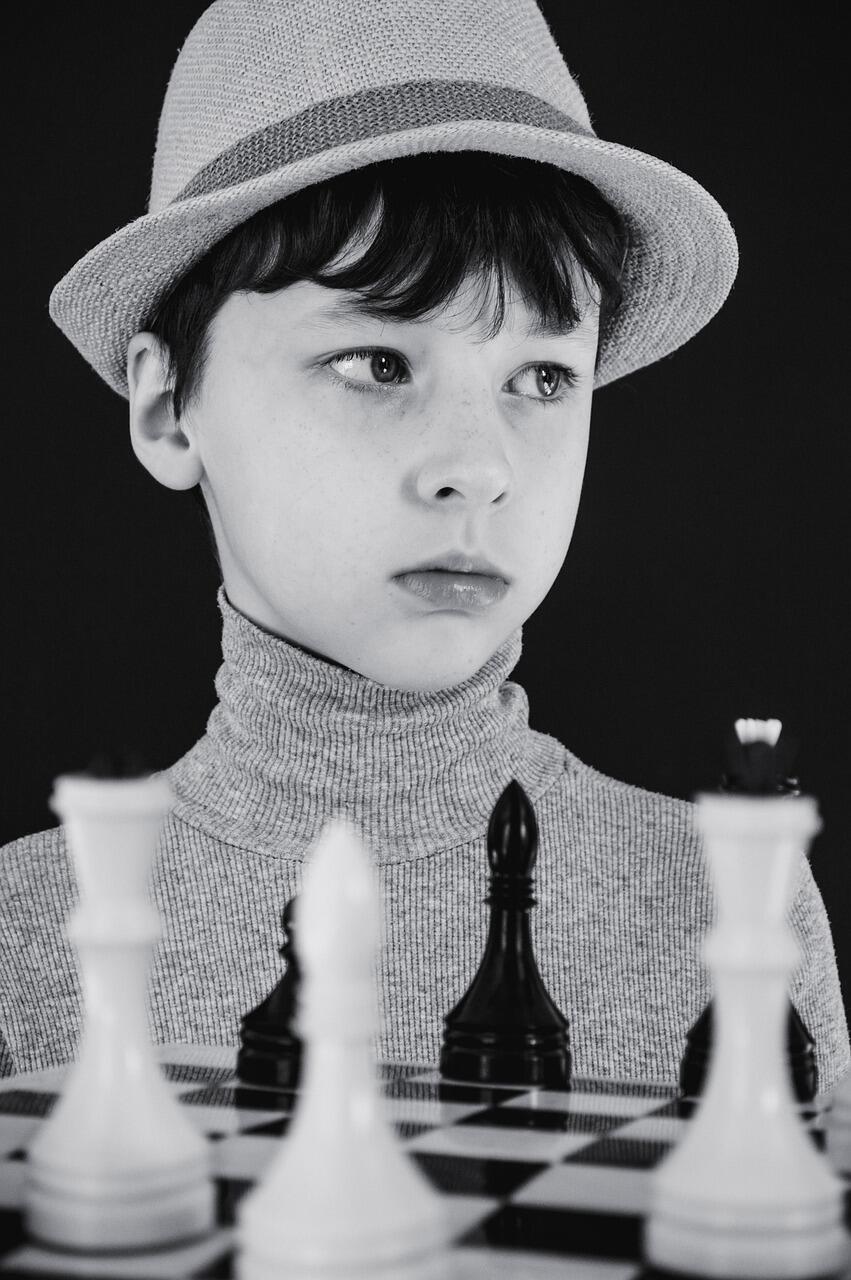 Czarno-białe zdjęcie chłopca w kapeluszu przy szachownicy