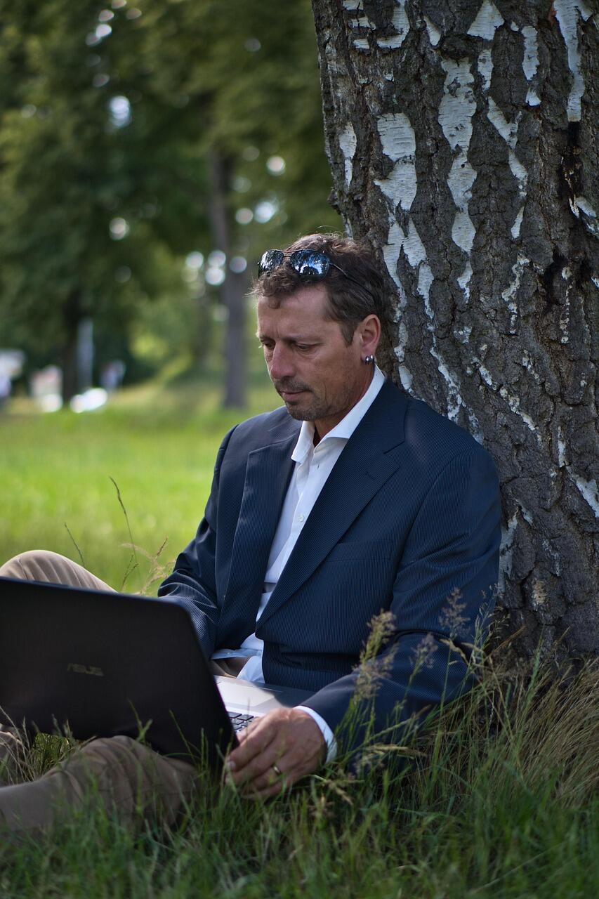 Mężczyzna siedzący pod drzewem z laptopem
