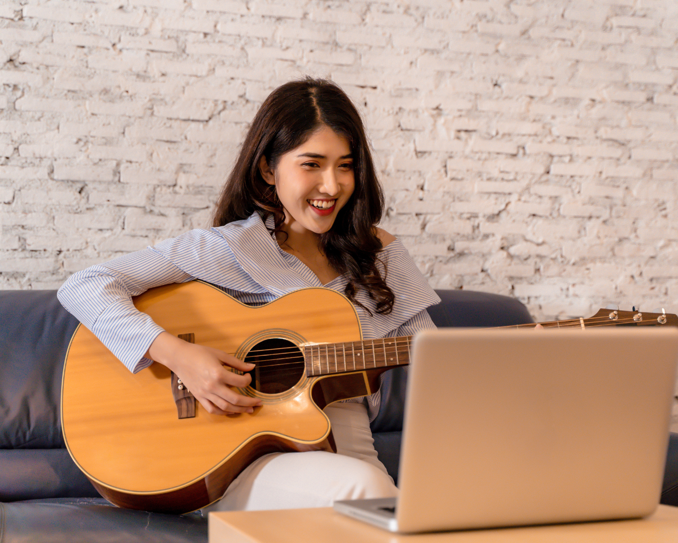 Osoba siedząca z gitarą akustyczną, skupiona na graniu, otoczona swobodną scenerią z miękkim, teksturowanym tłem ściany