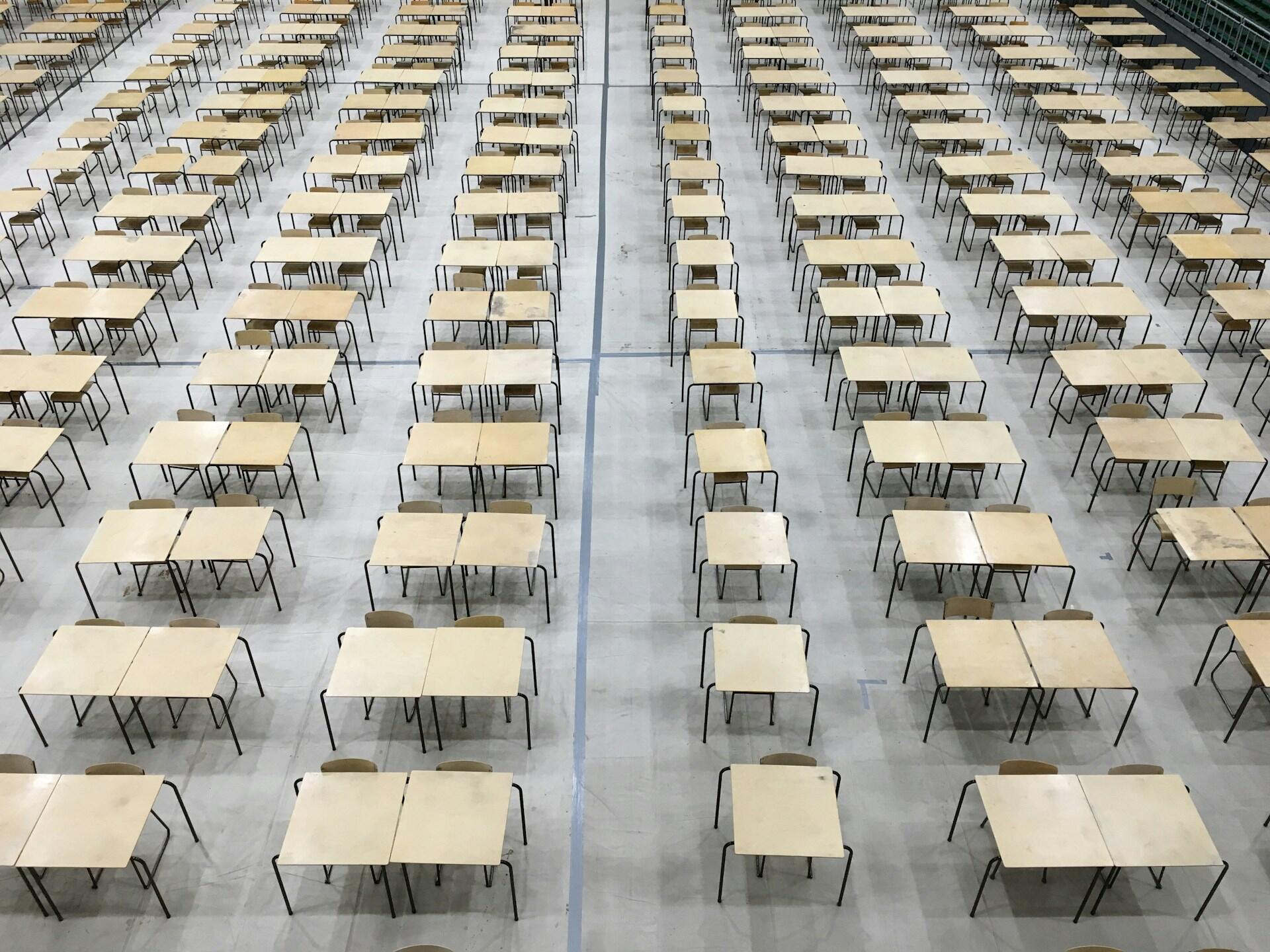 Stoliki ustawione w sali przeznaczonej do przeprowadzenia egzaminu maturalnego. Unsplash: Akshay Chauhan