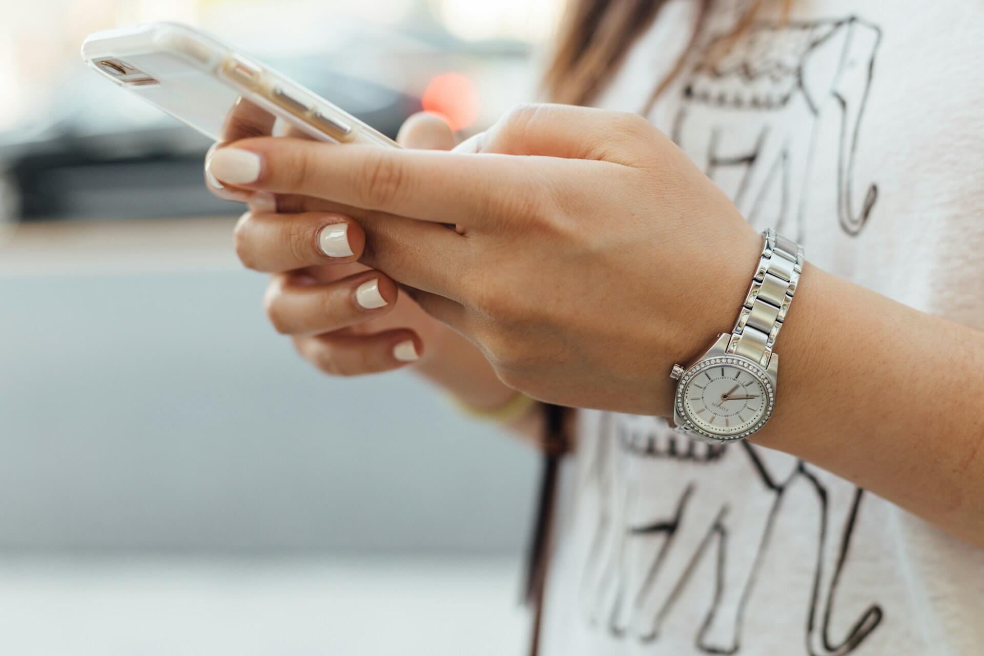 smartfon trzymany w dłoniach osoba pisze ma na przegubie klasyczny zegarek