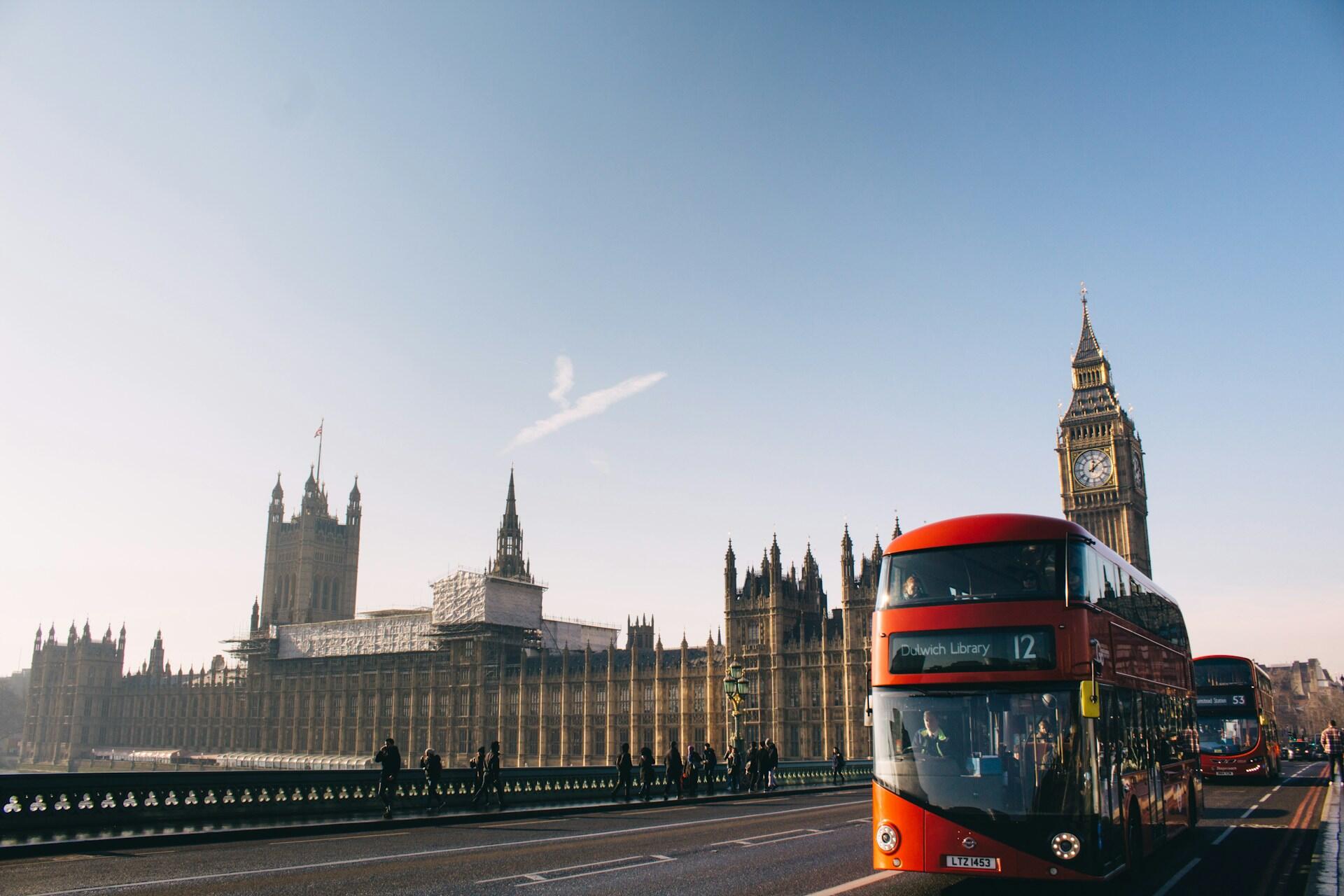 Czerwony piętrowy autobus przejeżdżający przez most Westminster Bridge, a w tle Big Ben i budynek Parlamentu w Londynie pod czystym, błękitnym niebem.