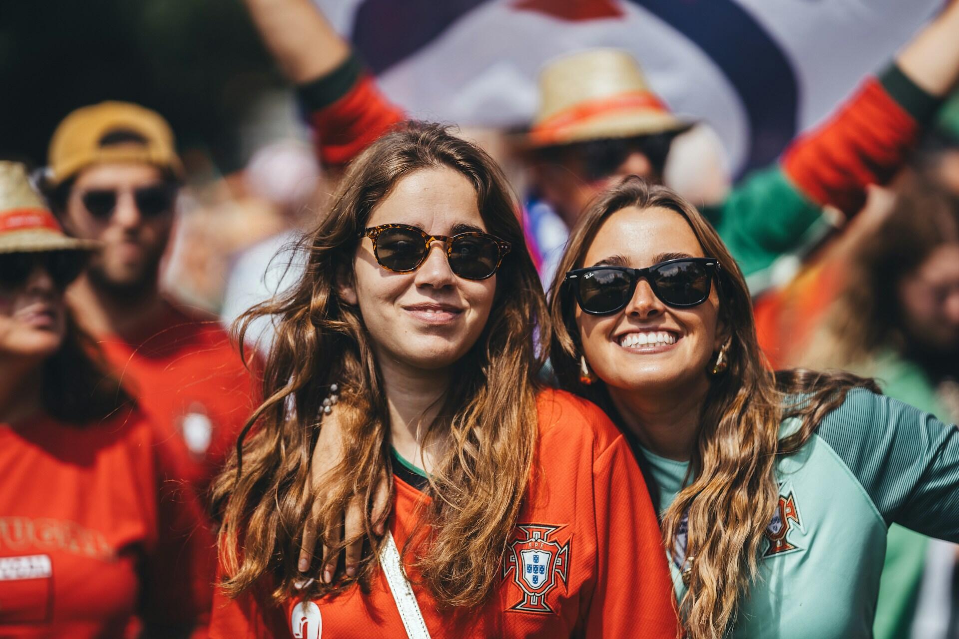 Grupa portugalskich kibiców piłkarskich w koszulkach reprezentacji, świętująca i dopingująca podczas imprezy na stadionie.