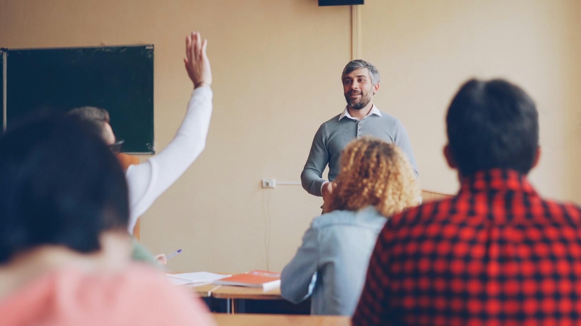 Nauczyciel prowadzi lekcję w szkole a jeden z uczniów zgłasza się do odpowiedzi podnoszą rękę