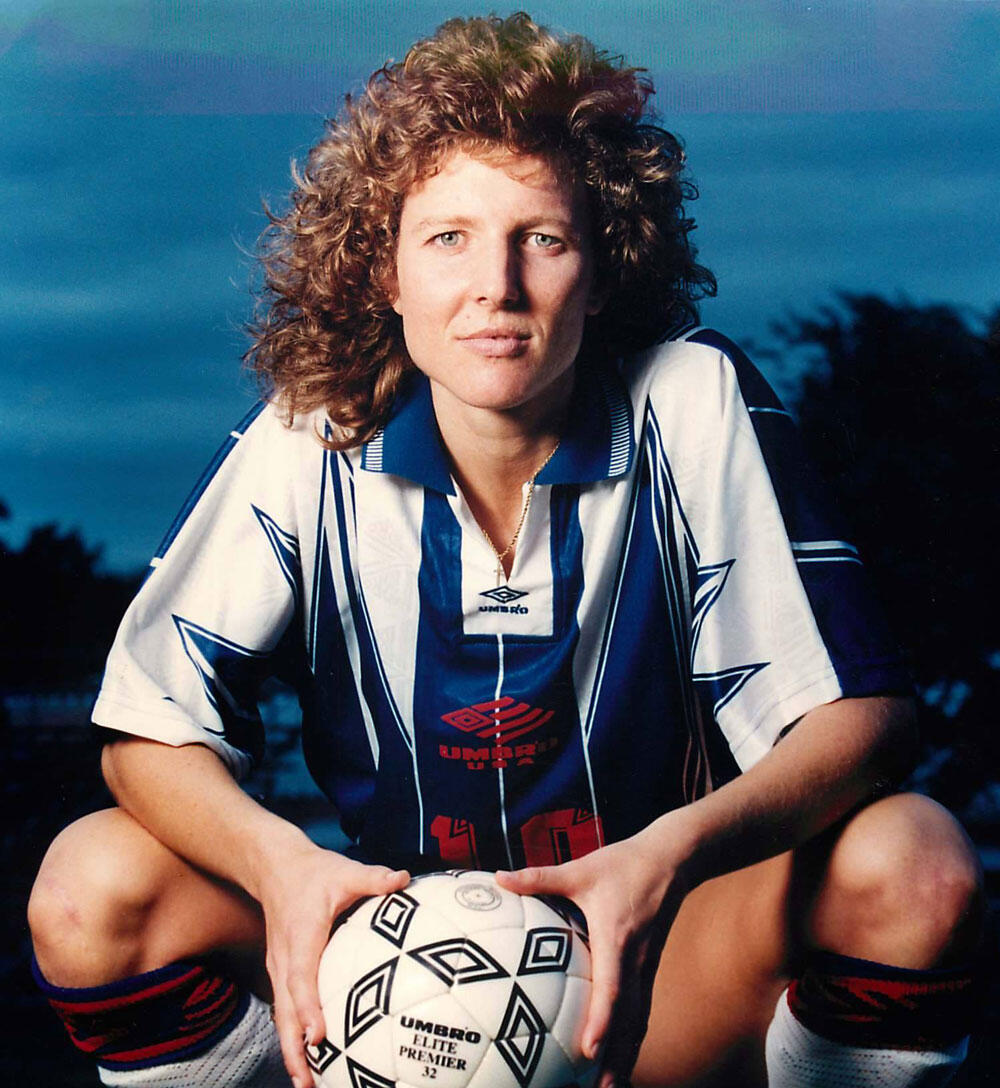 Młoda piłkarka w klasycznym stroju marki Umbro, kucająca i trzymająca czarno-białą piłkę Umbro Elite Premier.