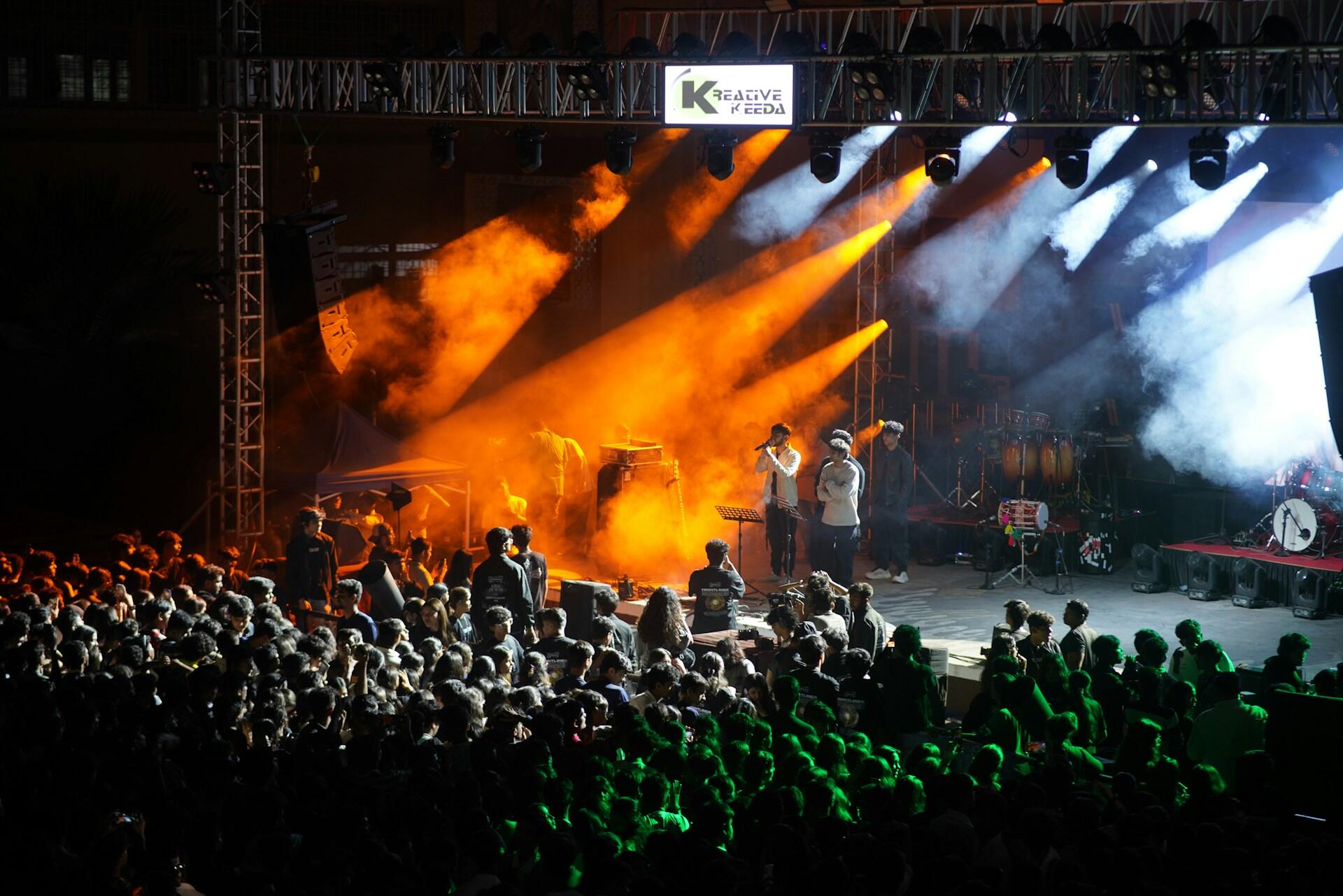 Koncert z artystami na oświetlonej na pomarańczowo scenie i publicznością. Unsplash: Pravin Shinde