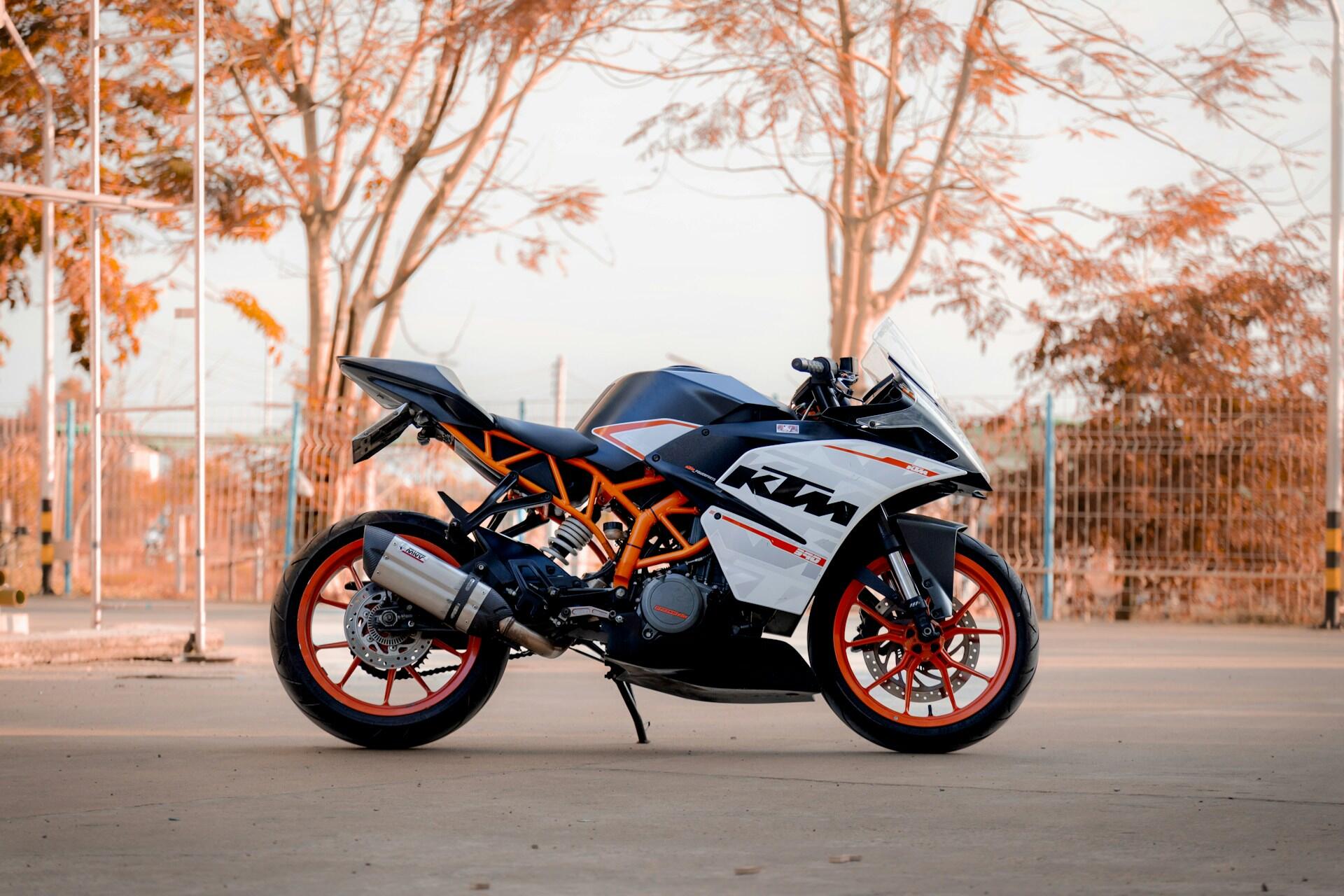 Motocykl sportowy stojący na placu na tle jesiennych drzew. Unsplash: Dom Puc