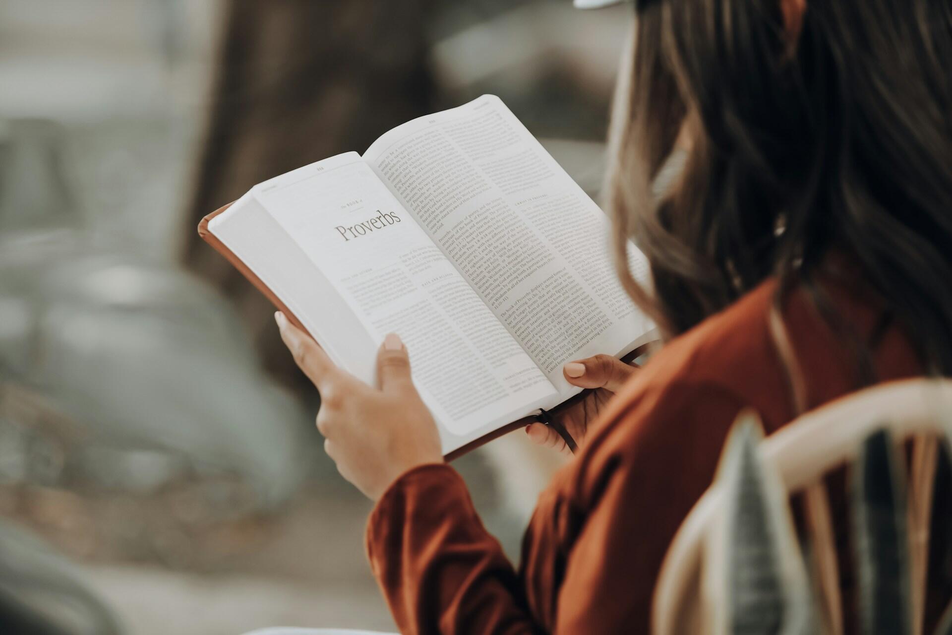 Kobieta czyta książkę otwartą na rozdziale "Proverbs" (przysłowia). Unsplash: Joel Muniz