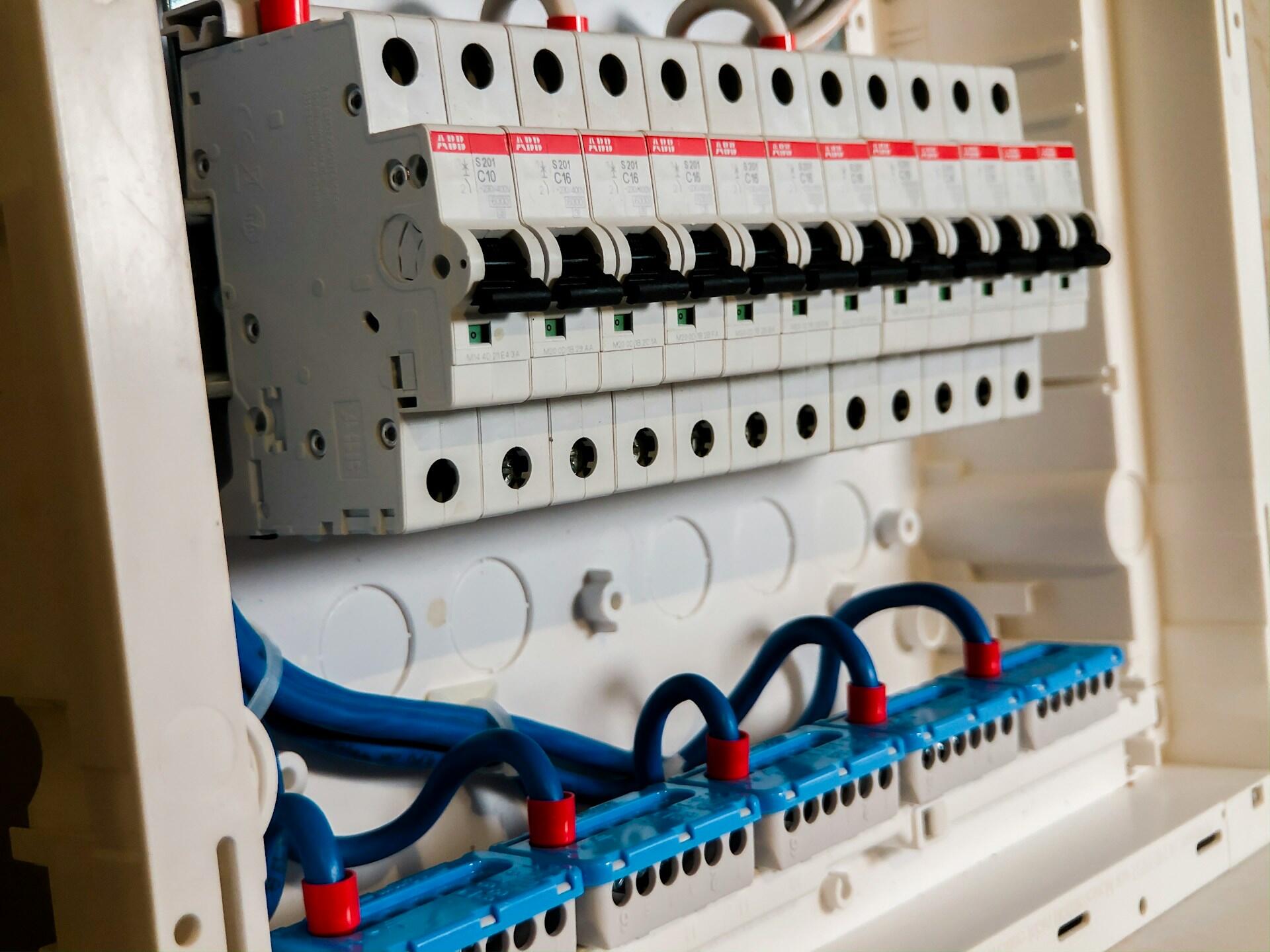 Domowa rozdzielnica elektryczna (skrzynka bezpiecznikowa / rozdzielnia) z górnym rządem bezpieczników, okablowaniem i złączami oraz białą obudową.