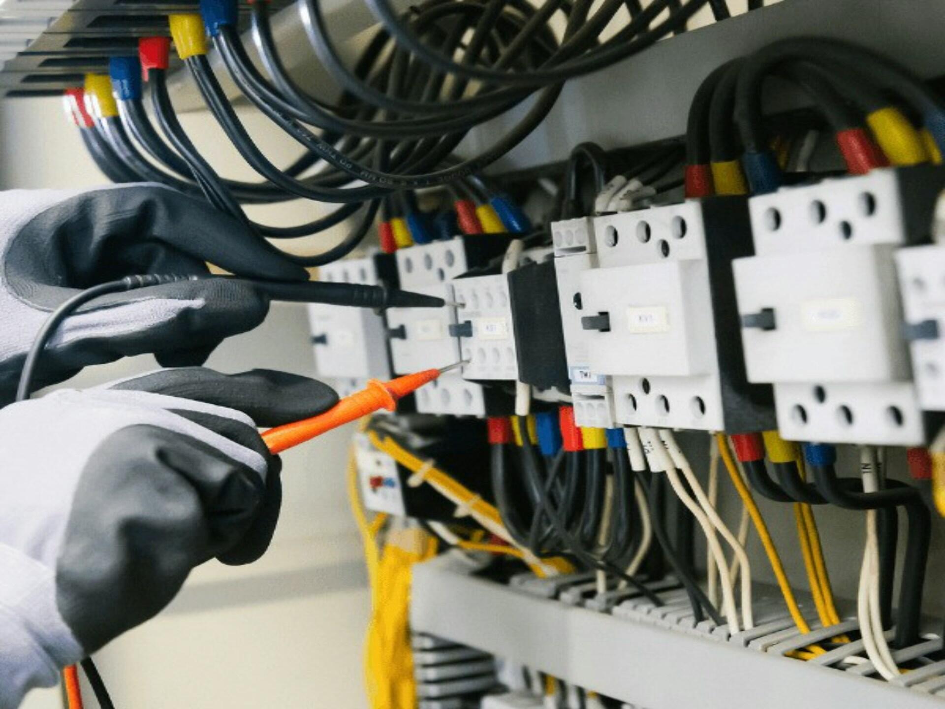Elektryk testuje urządzenia elektryczne i okablowanie wewnątrz panelu sterowania.