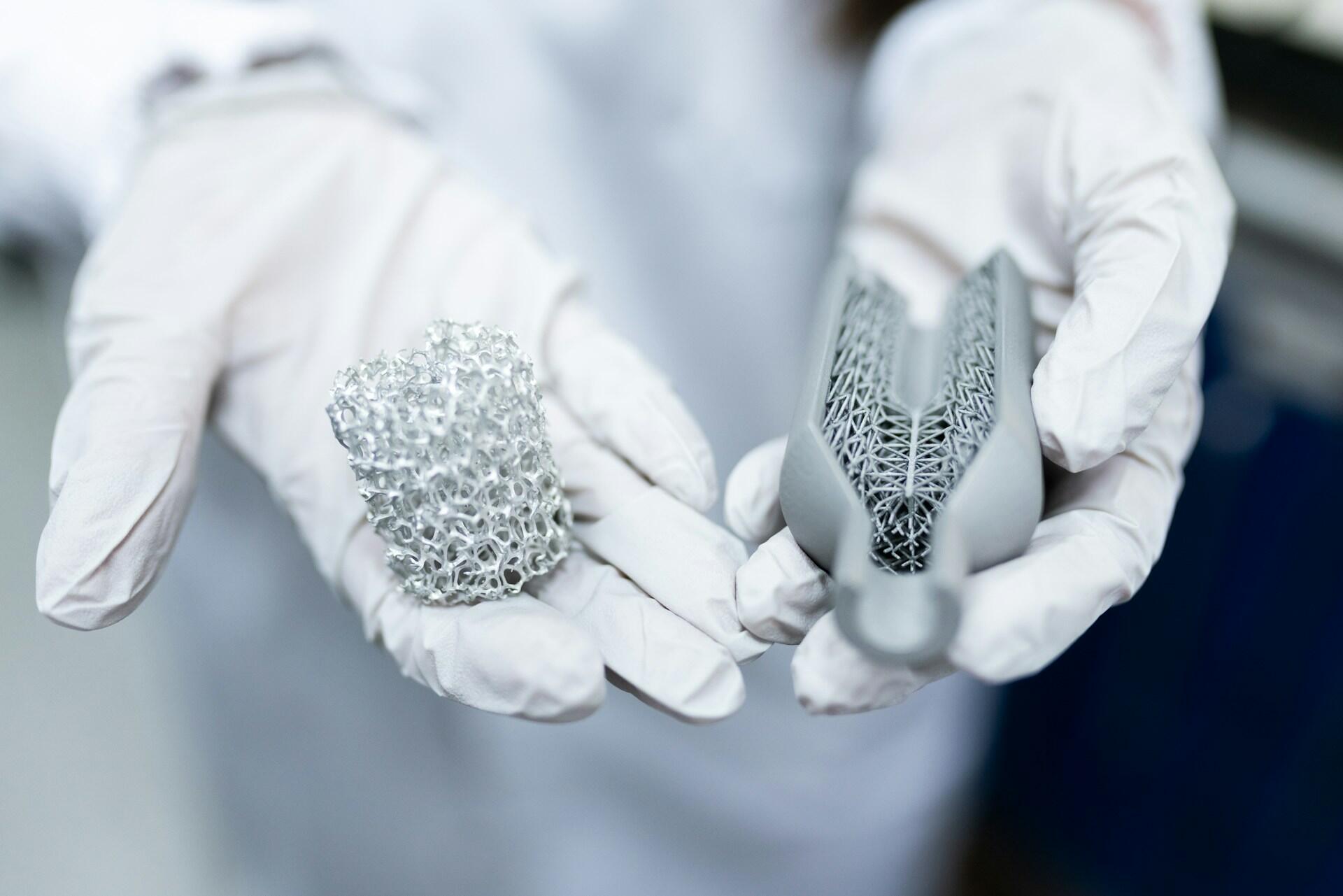 Na dłoniach w białych rękawiczkach ochronnych leżą dwa zaawansowane elementy inżynieryjne wykonane w nowoczesnych technologiach materiałowych.