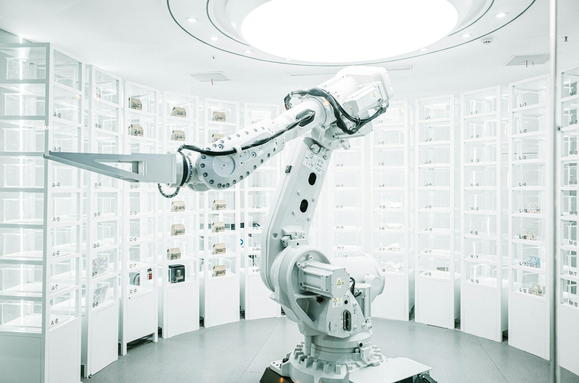 Nowoczesne ultra-czyste pomieszczenie (przypominające zaawansowane laboratorium, zautomatyzowany magazyn lub showroom technologiczny) z dużym przemysłowym ramieniem robotycznym. Unsplash: ZHENYU LUO