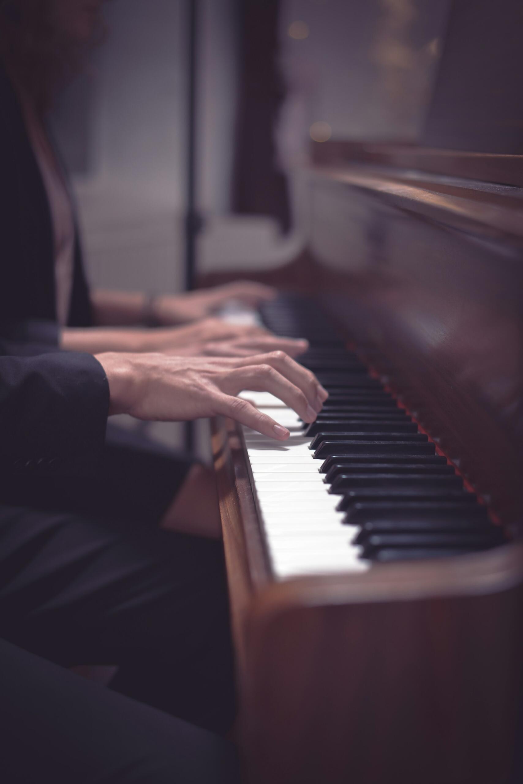 Dwie osoby grają razem w duecie (na cztery ręce) na jednym pianinie w klasycznej, drewnianej obudowie. Unsplash: Kiwihug