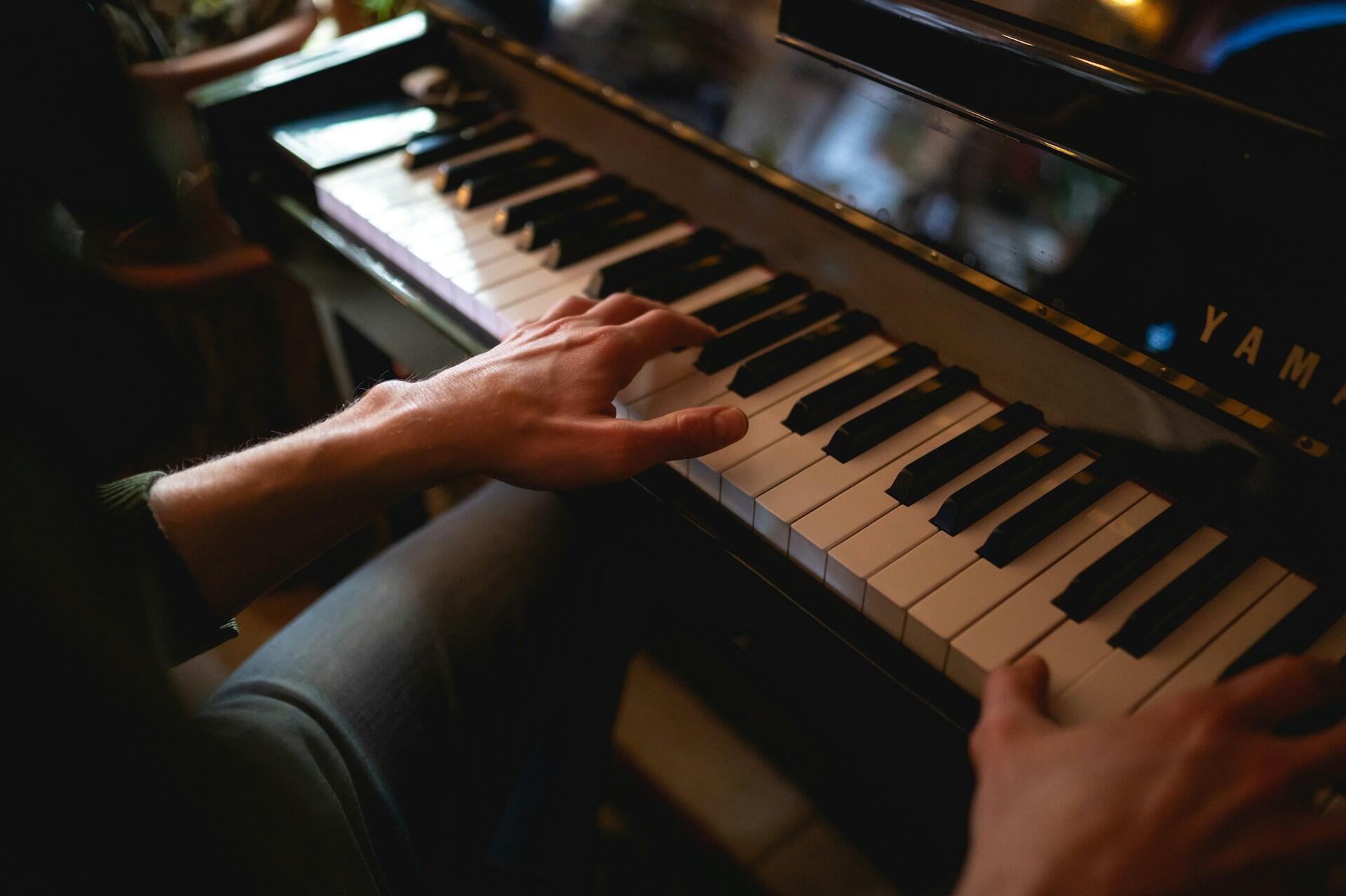 Dłonie mężczyzny grającego na czarnym, lakierowanym pianinie marki Yamaha.