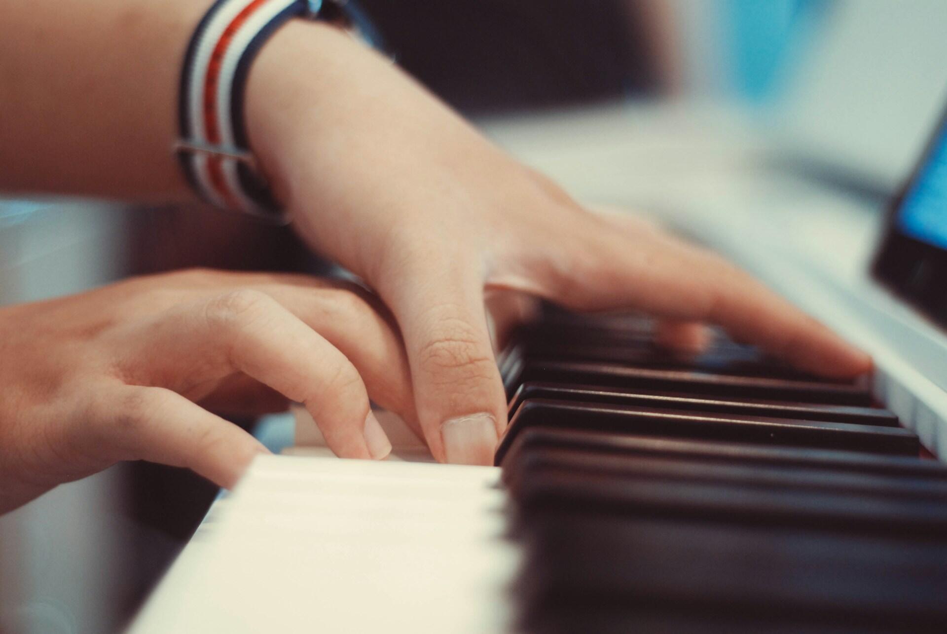 Zbliżenie na palce osób grających na pianinie. Unsplash: Ai Nhan