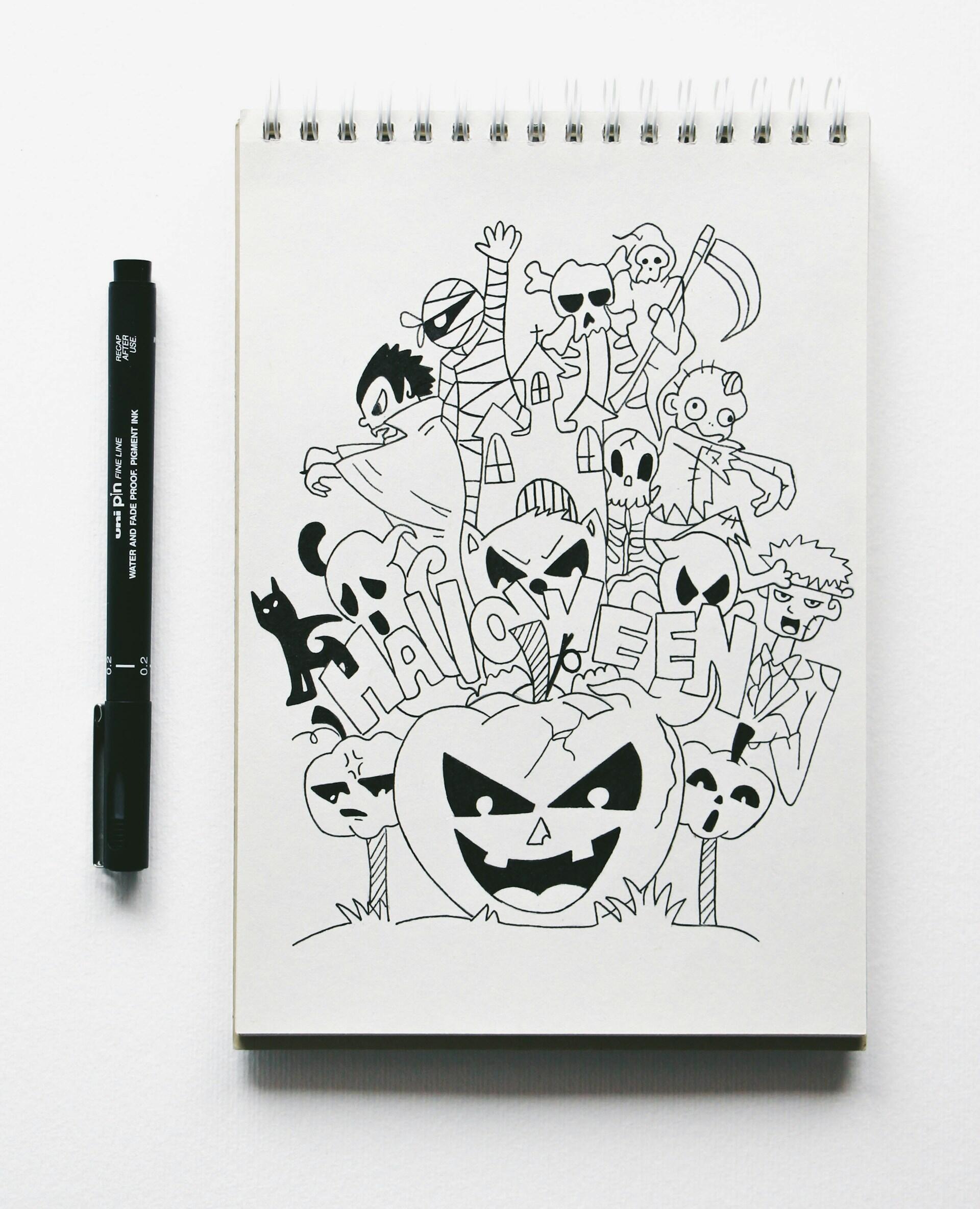 Szkicownik ze spiralą z czarno-białym rysunkiem nawiązującym do Halloween, a obok leży czarny cienkopis.