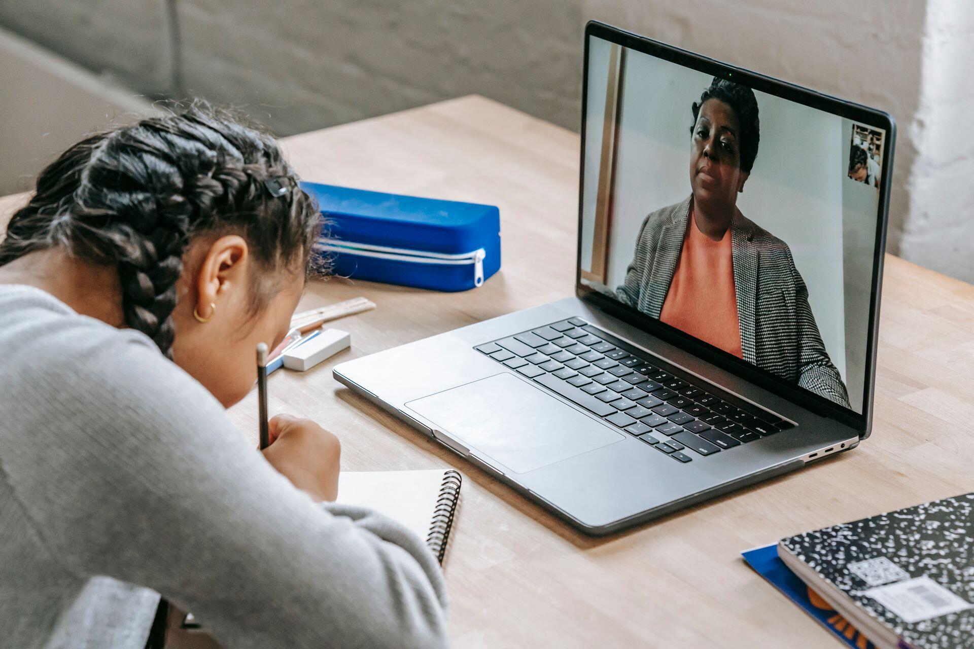 professora em ecrã de computador e aluna a escrever