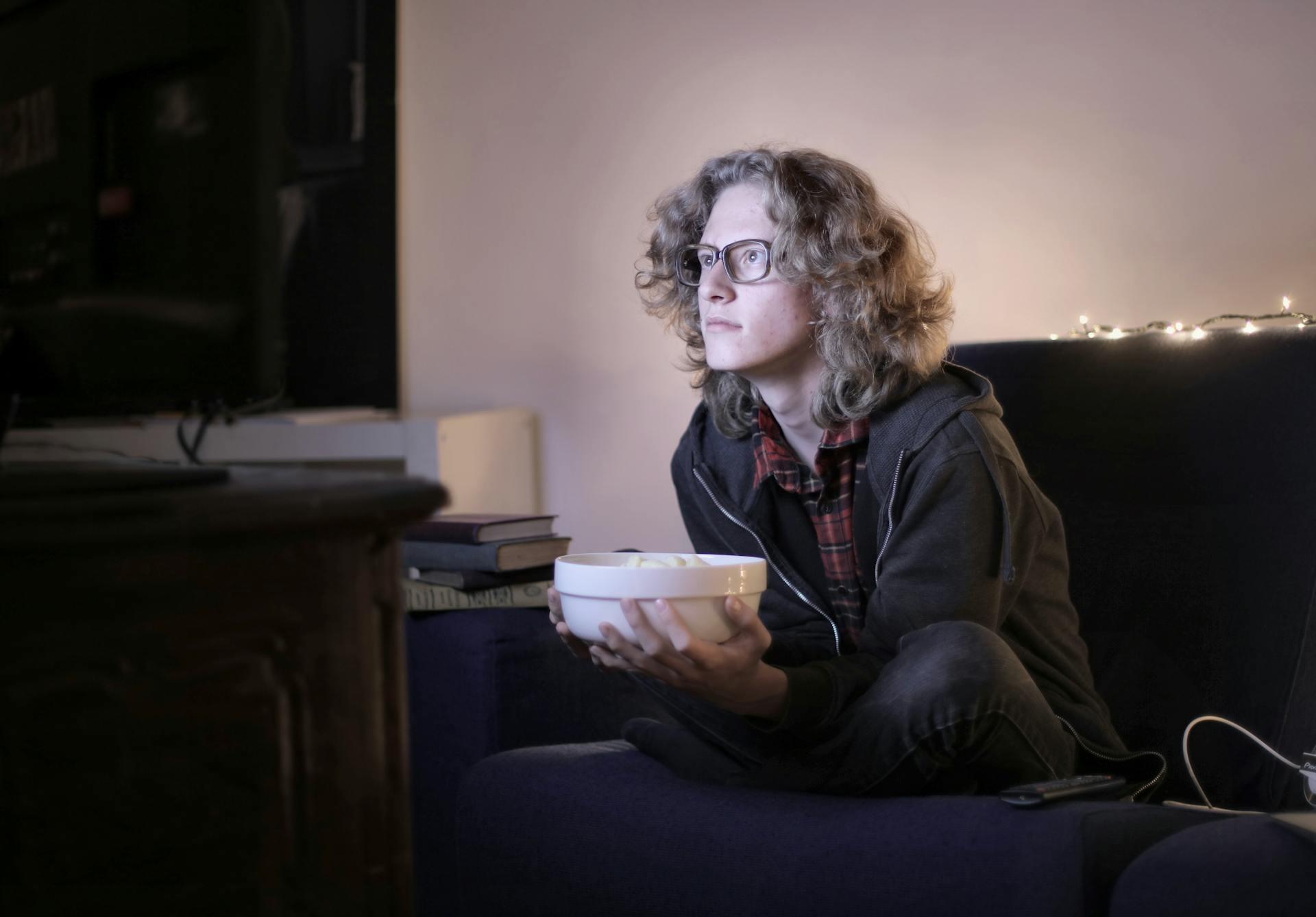 pessoa de óculos com taça de pipocas e ver tv