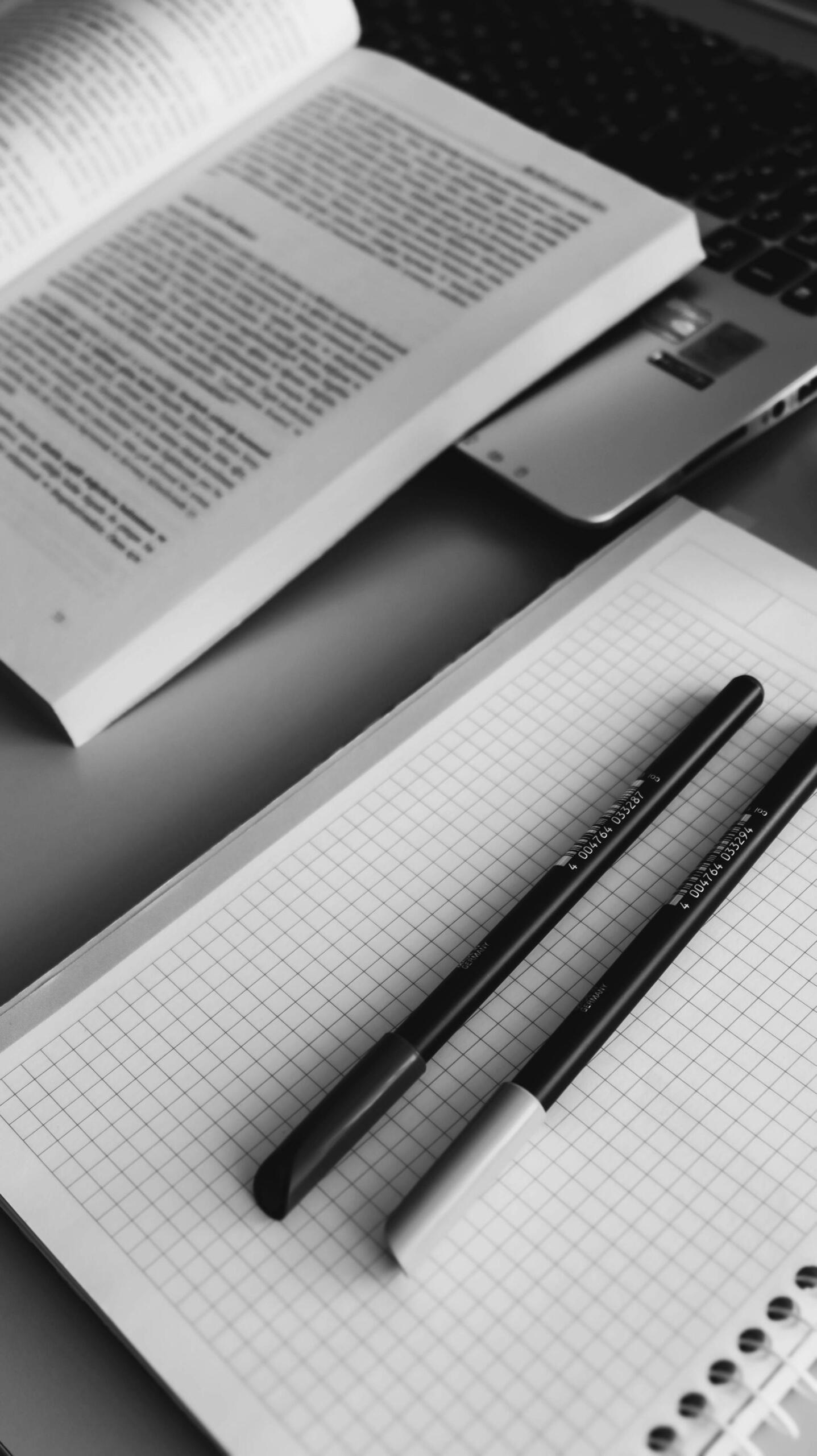 caderno quadriculado, canetas e livro
