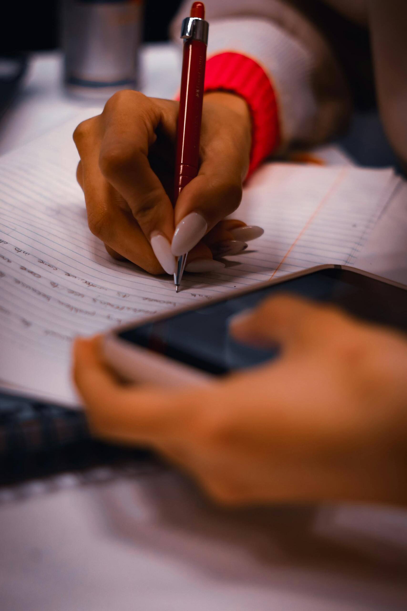 pessoa com telemóvel na mão e a escrever