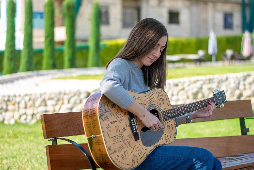 Jovem mulher toca guitarra num jardim do Porto