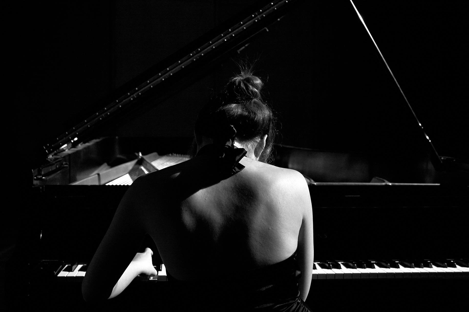 Uma pianista, sentada em frente a um piano de cauda, durante um concerto.
