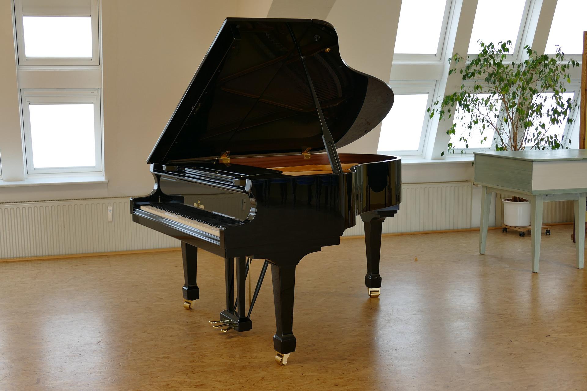 Um piano de cauda preto, com a tampa aberta, numa sala vazia.