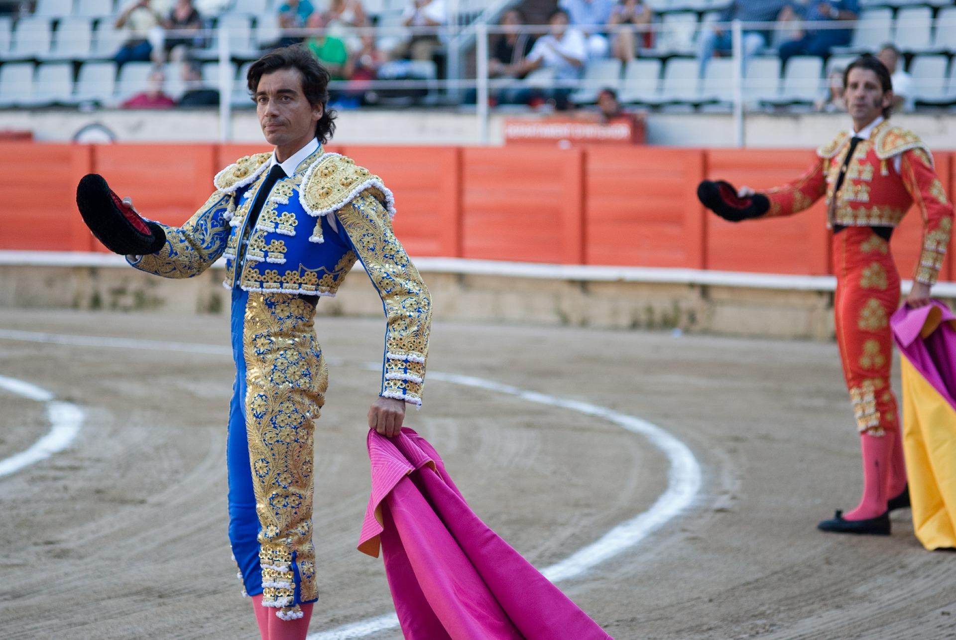 Dois toureiros espanhóis, tradicionalmente trajados, numa praça de touros.
