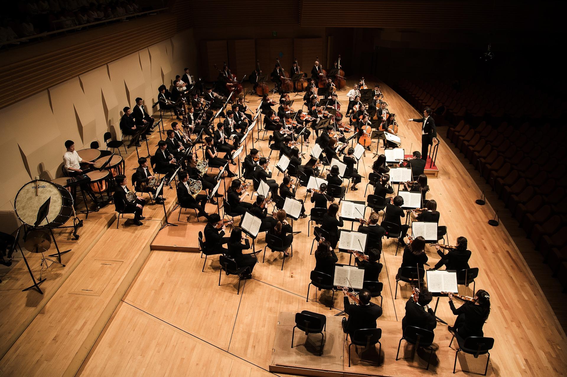Uma orquestra e um maestro, num palco, a preparar um concerto.