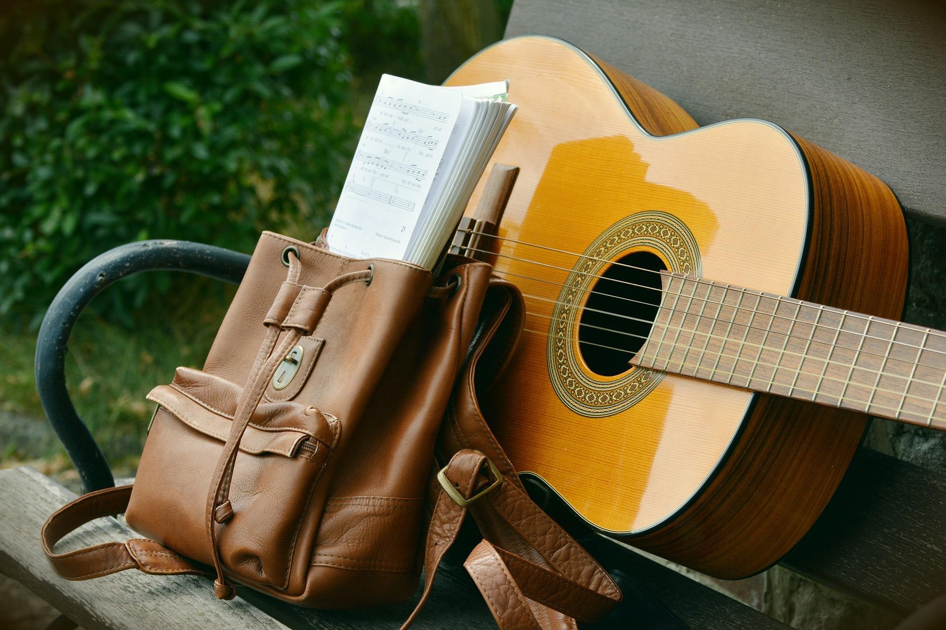 Uma mochila com uma partitura e uma guitarra pousadas no banco de jardim.