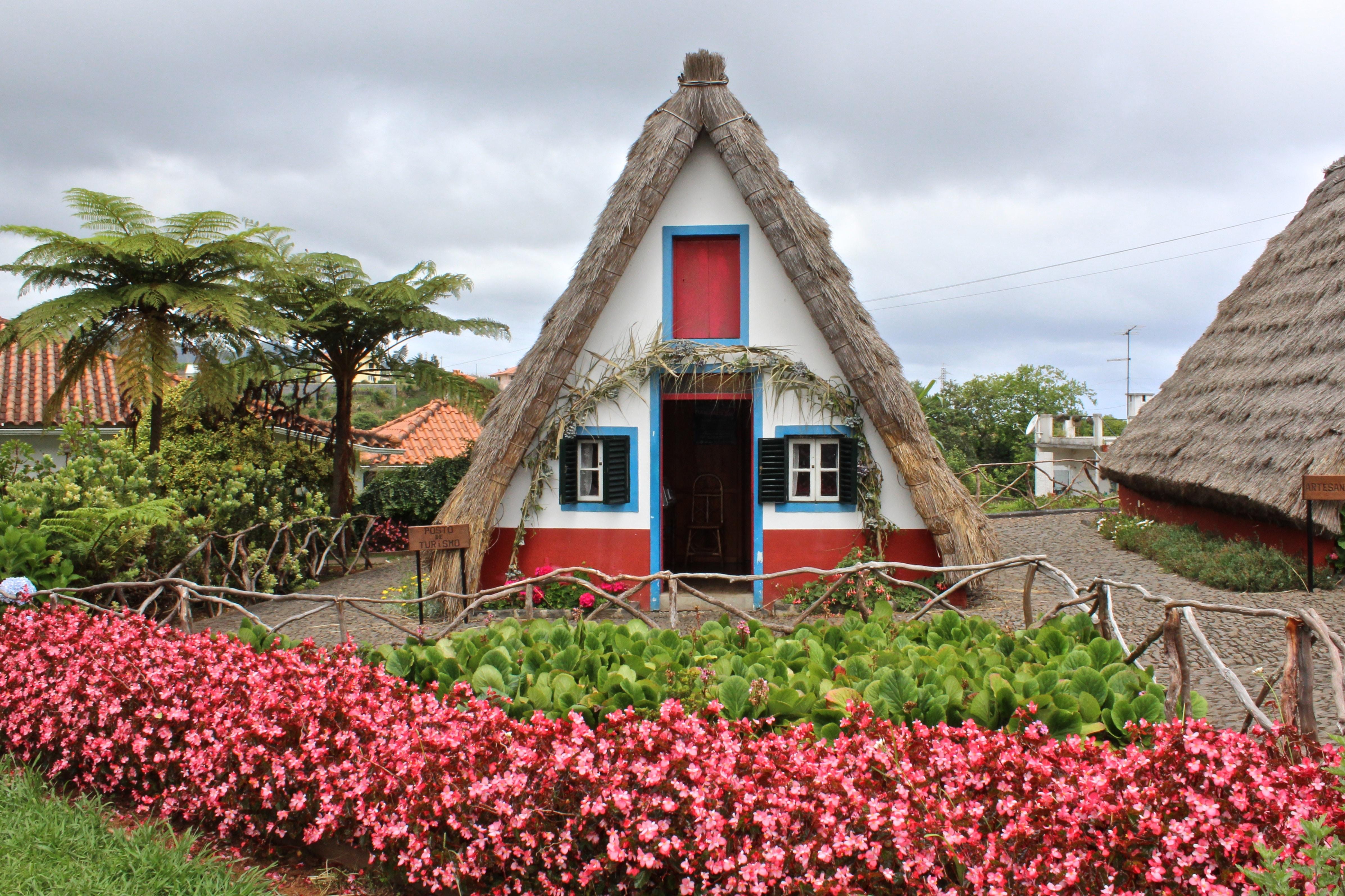 Casa triangular, típica do concelho de Santana, na Madeira, rodeada de um jardim colorido.