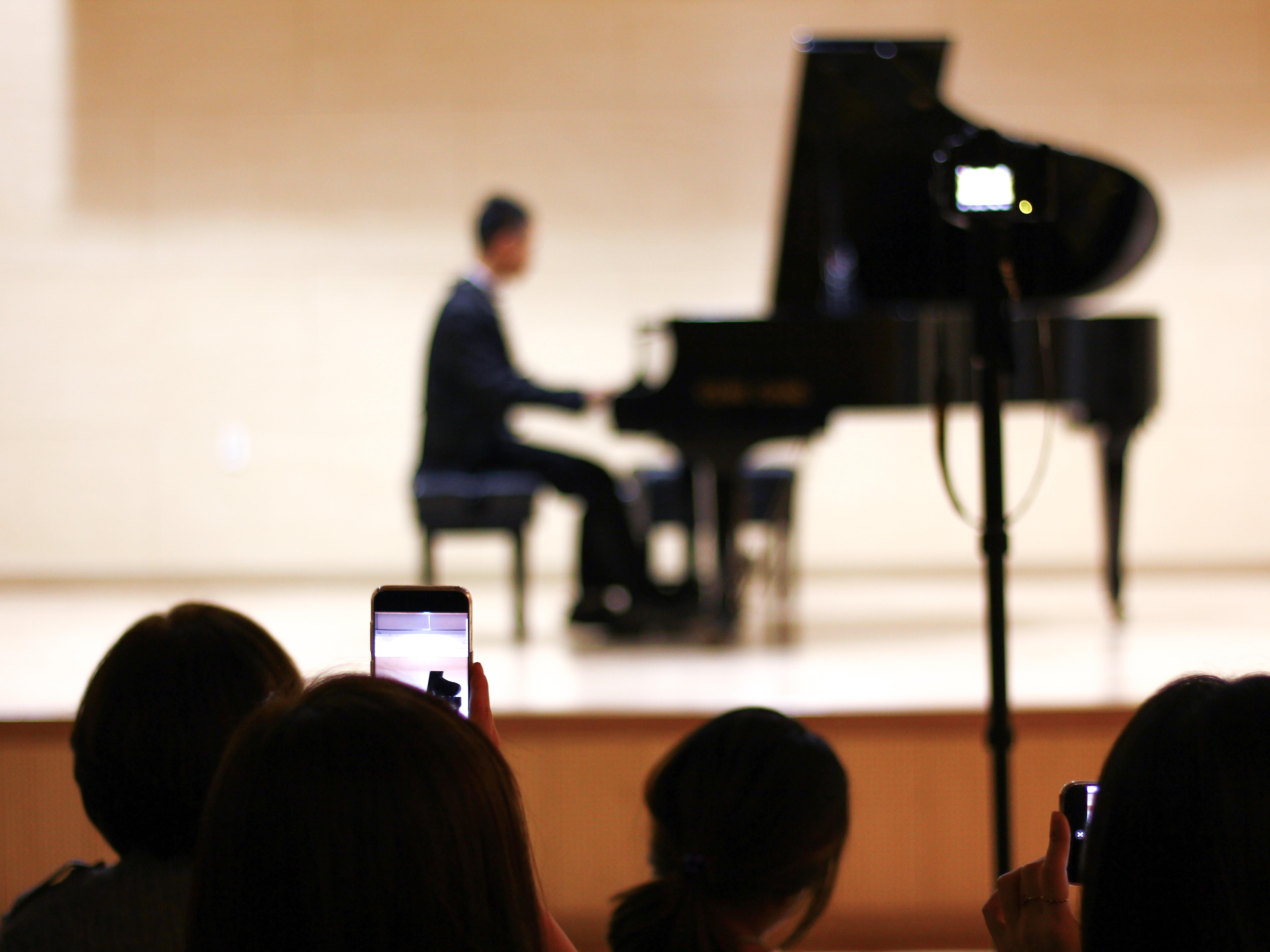 Um homem ao piano, num palco, acompanhado por uma audiência.