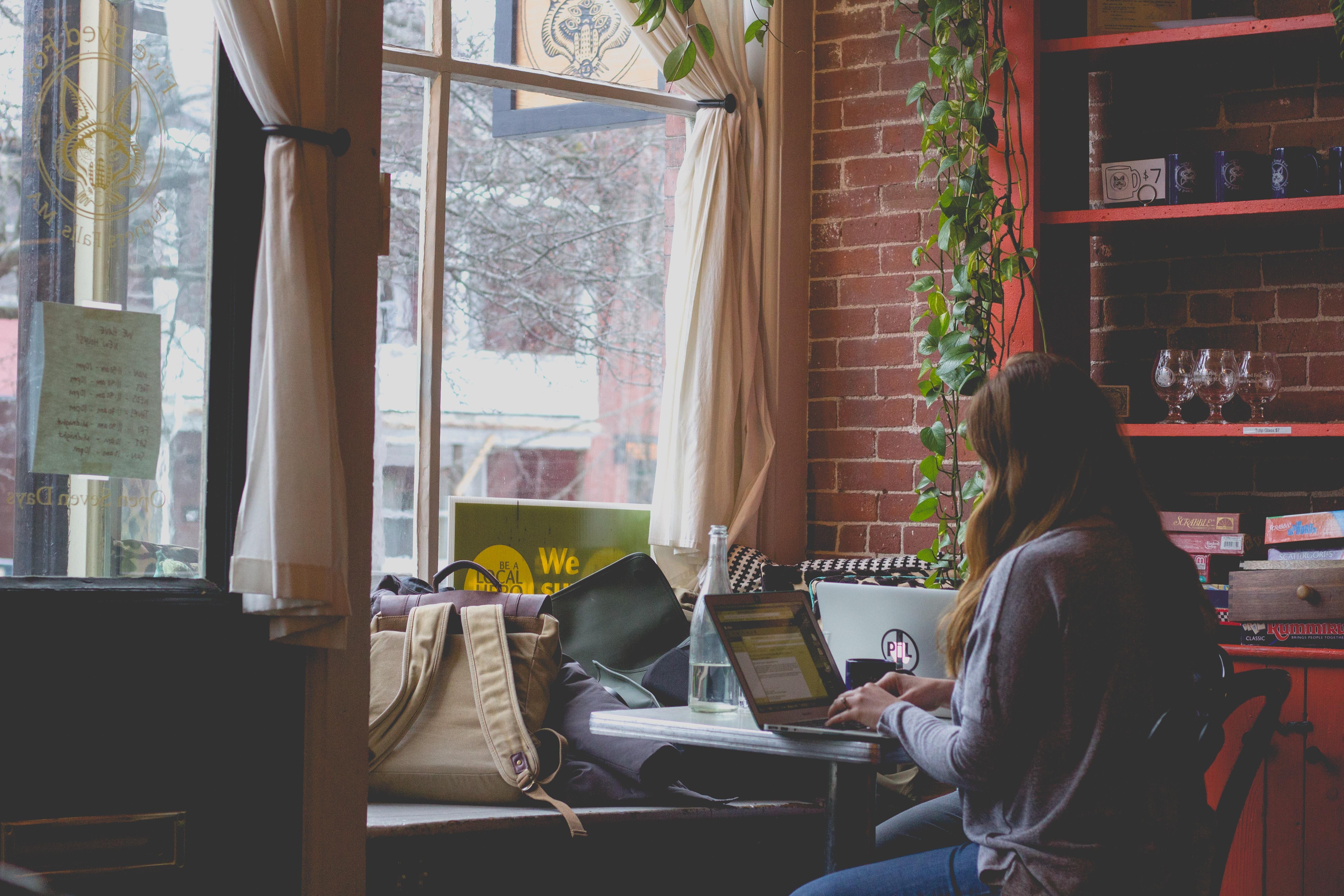 Uma rapariga num café, junto à janela, com o computador portátil a estudar espanhol.
