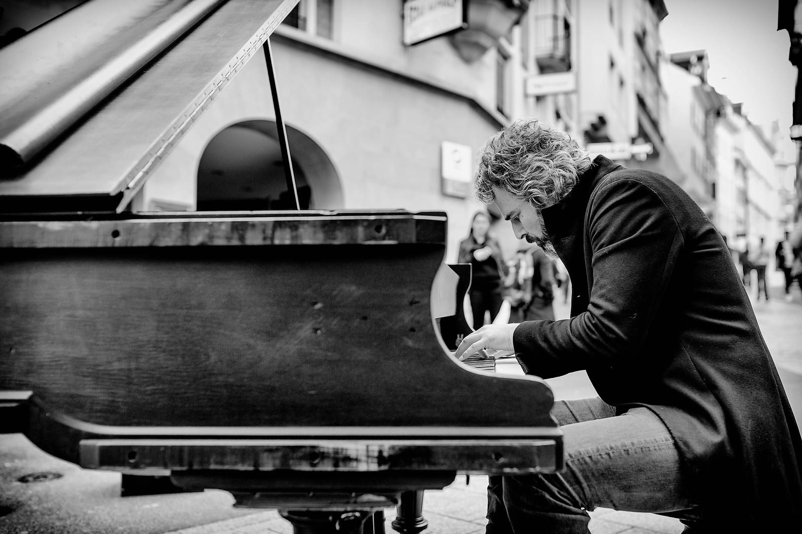 Fotografia a preto e branco de um homem a tocar piano na rua.