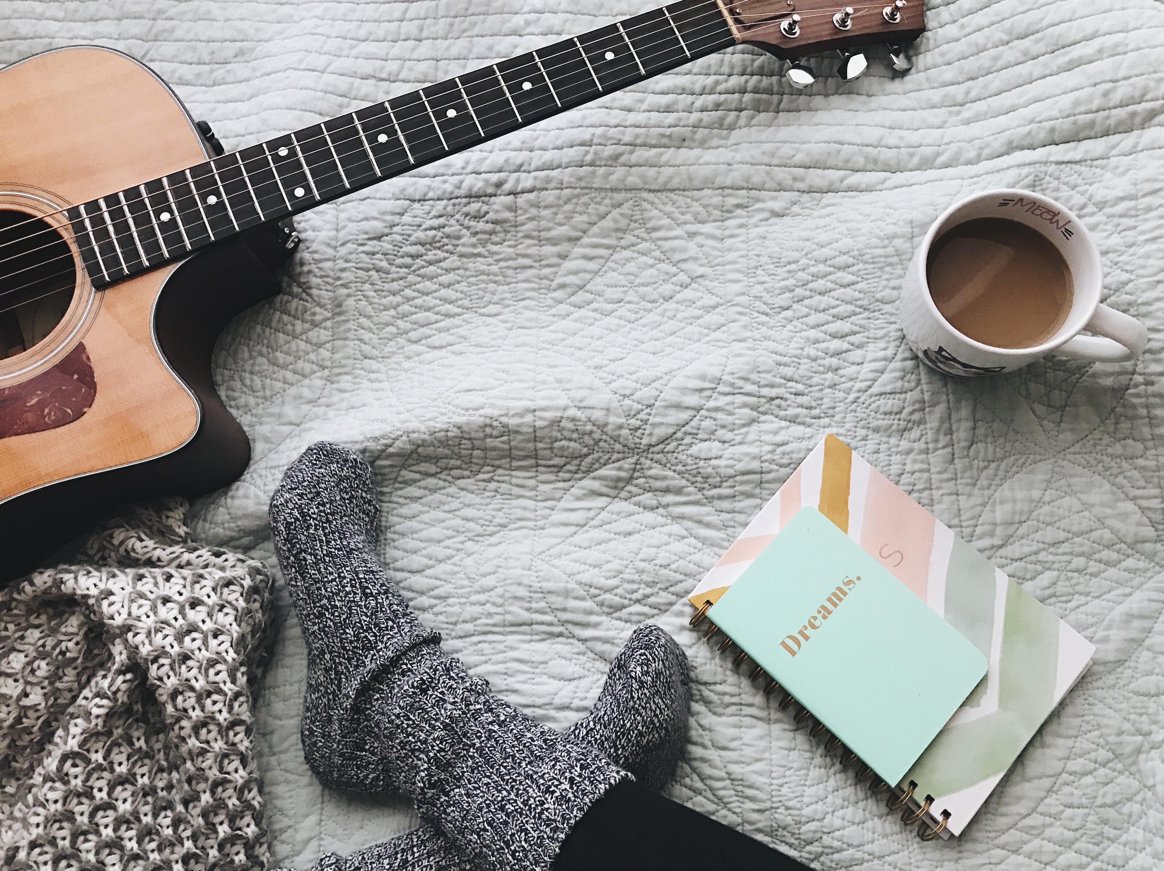 Guitarra, pés com meias, cadernos e chávena