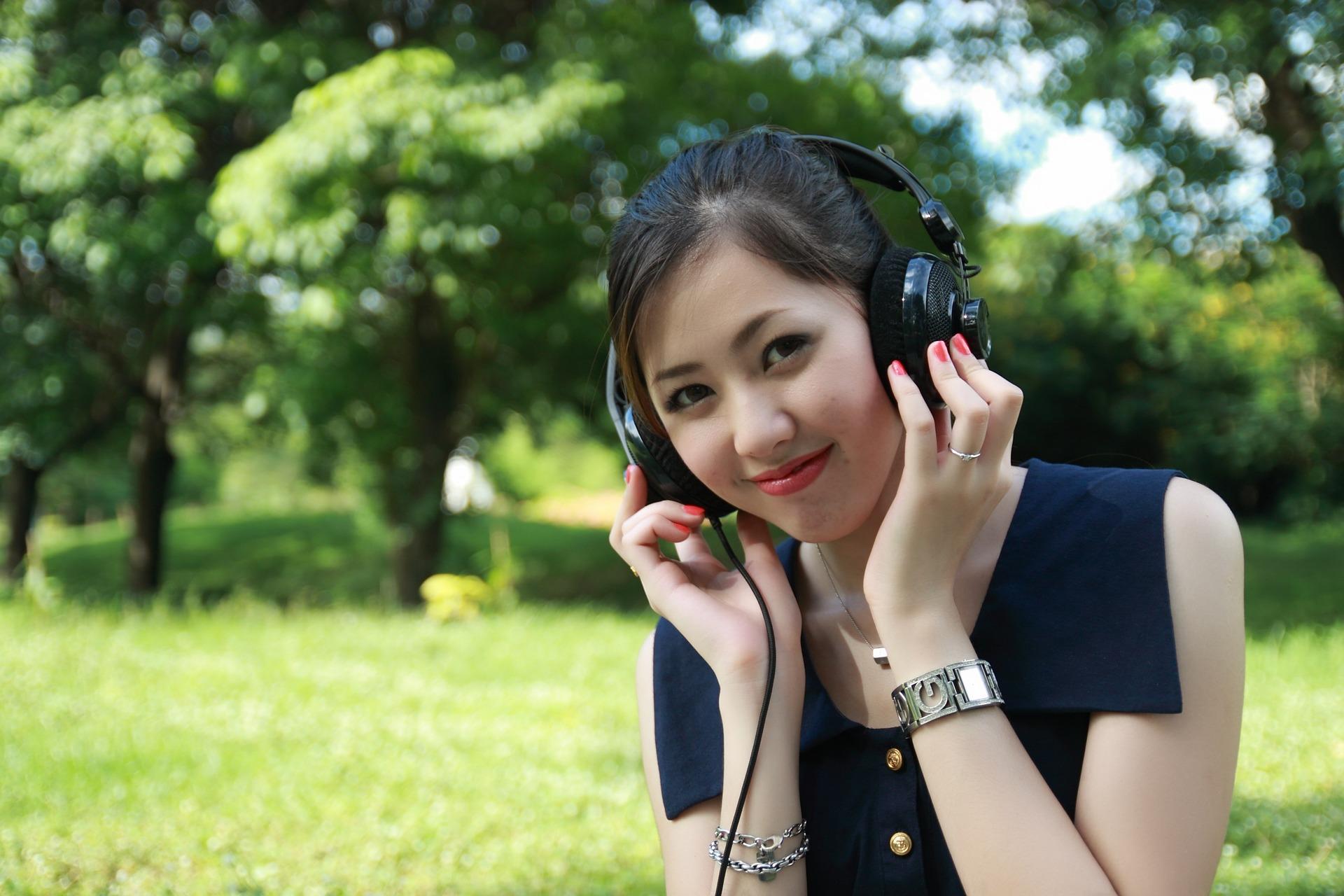 Uma rapariga sentada no parque, a ouvir musica com uns headphones.