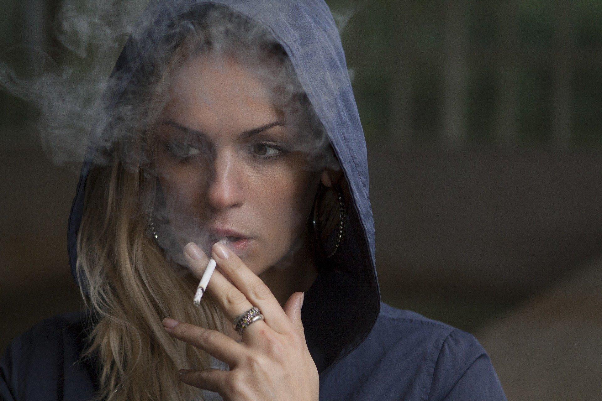 Uma rapariga, com um capuz posto, a fumar um cigarro.