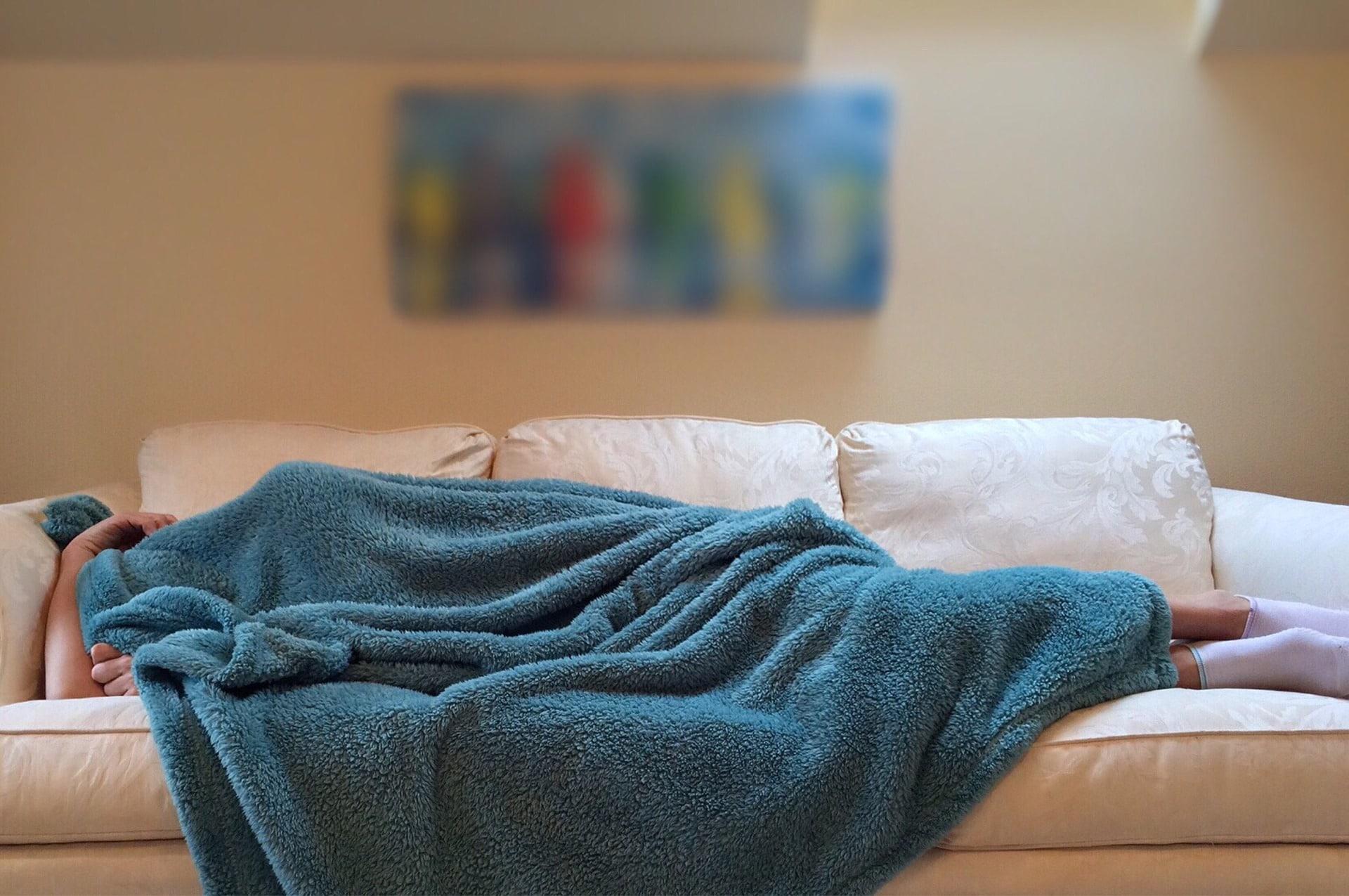 Uma rapariga, tapada por uma manta azul, a dormir no sofá.