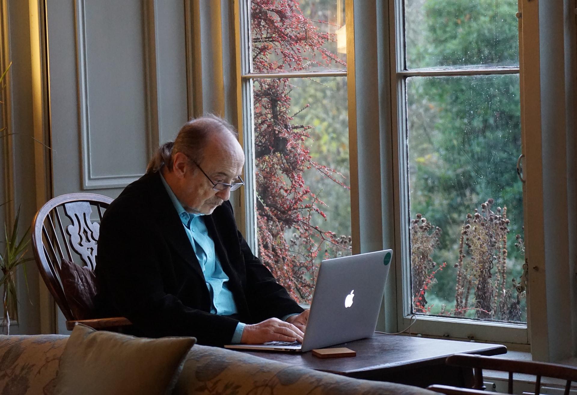 pessoa idosa usando computador perto da janela 
