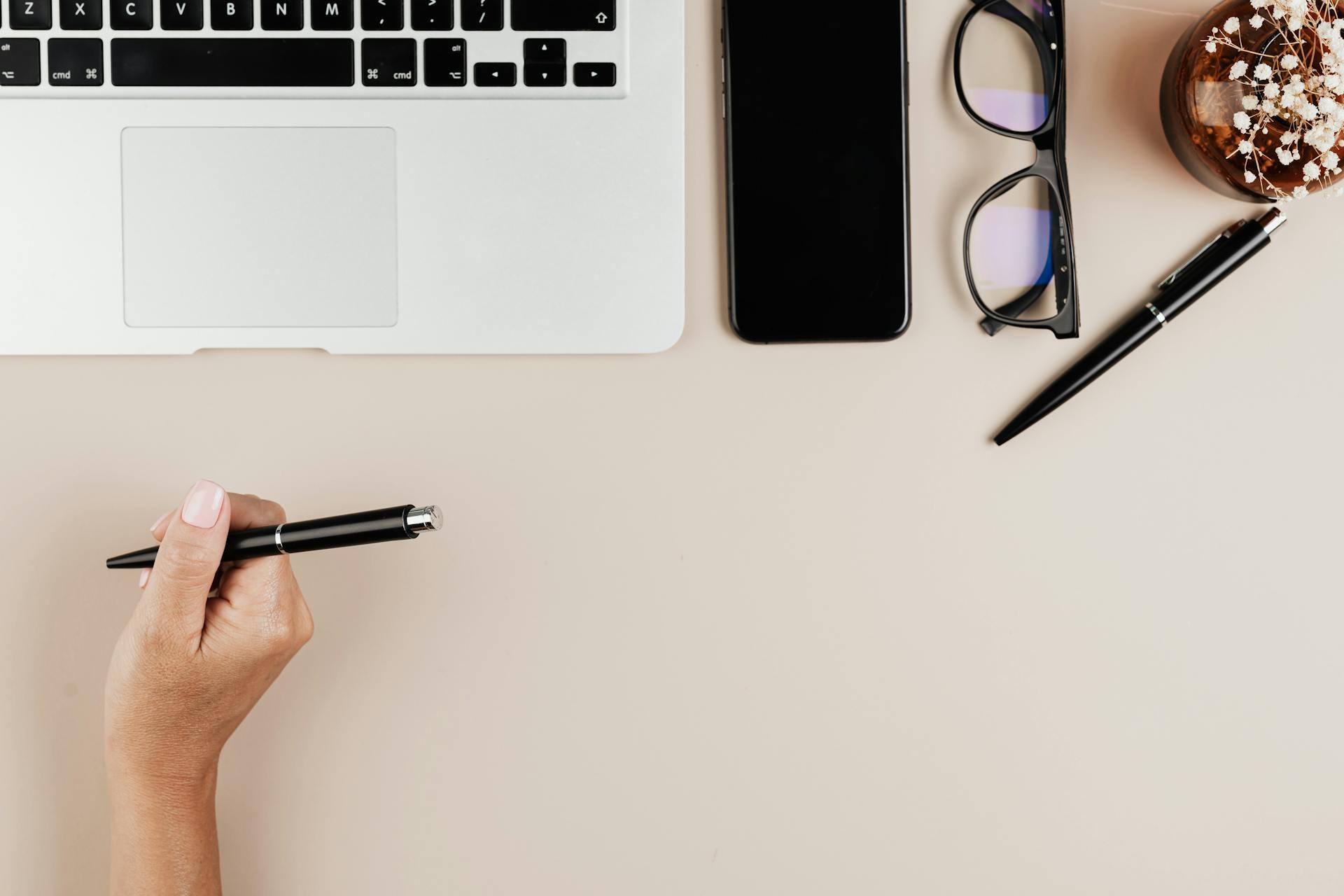 pessoa com caneta na mão, computador e telemóvel