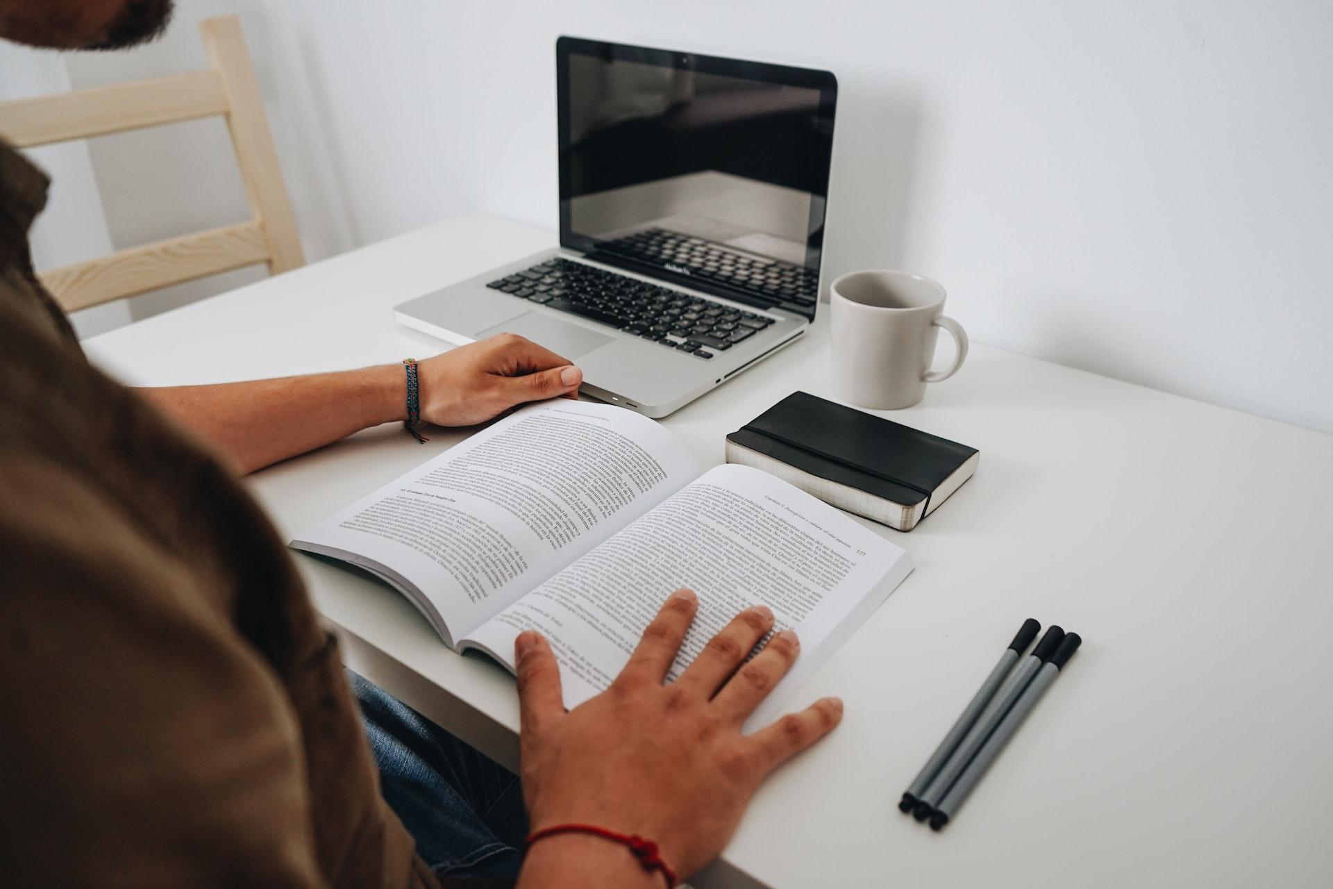 pessoa com livro aberto e canetas