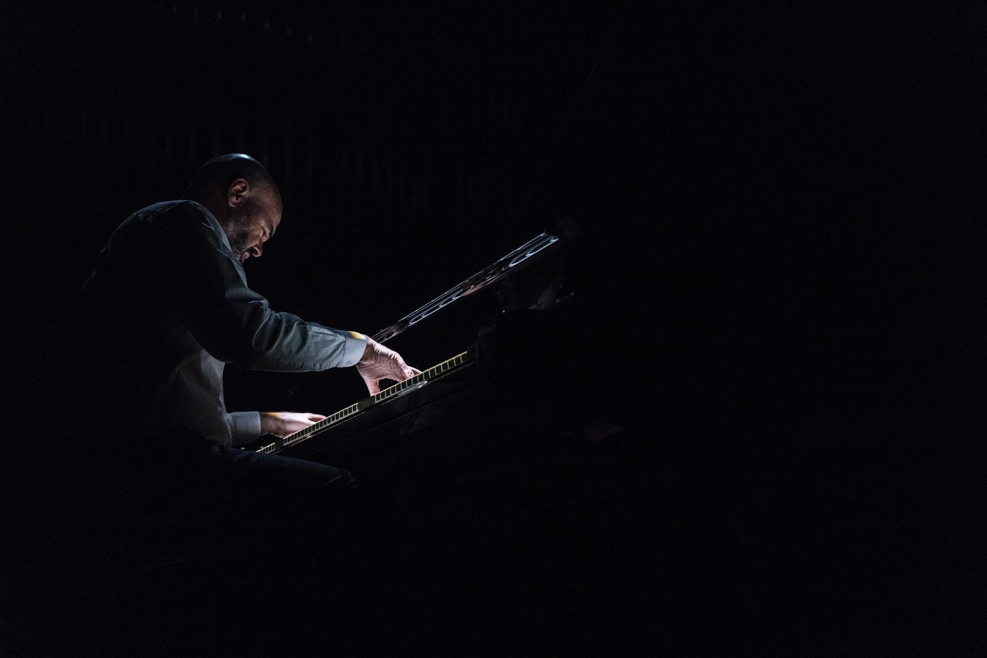 Homem a tocar no piano num ambiente escuro