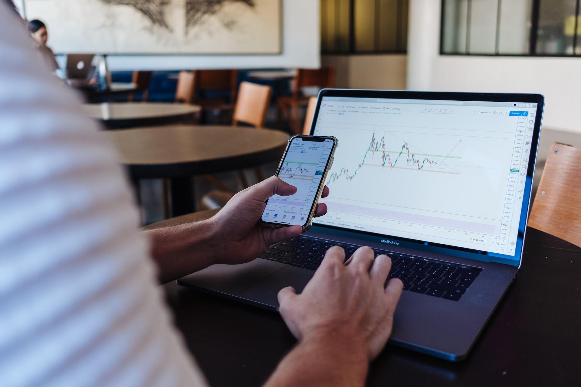 Mão a segurar telemóvel e com computador à frente