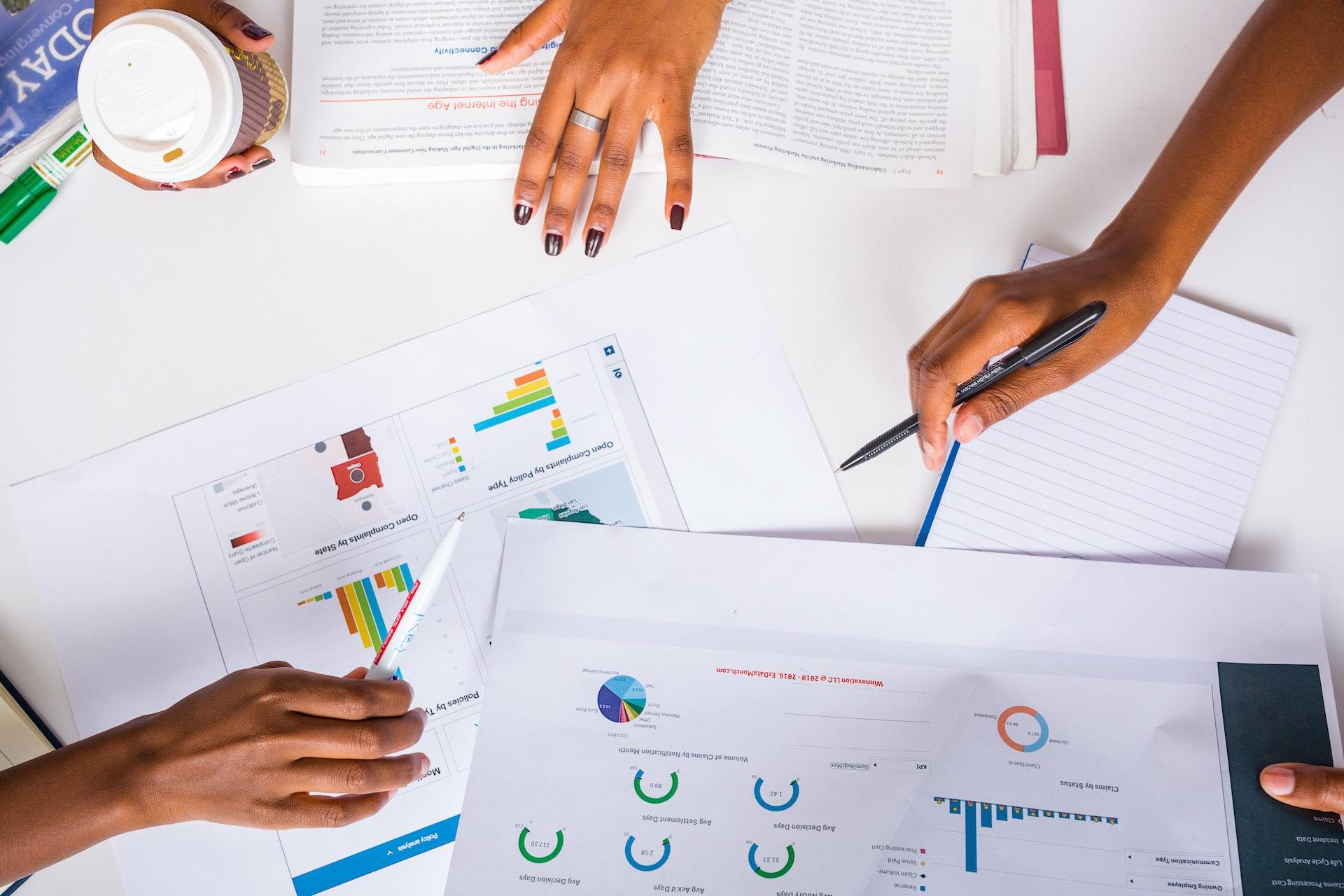 papeis com graficos e varias maos de pessoas